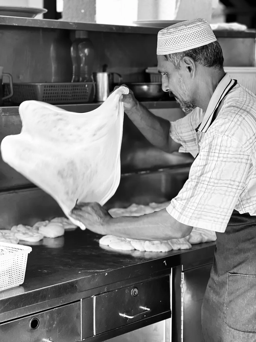 Cook tossing and stretching thin roti canai dough in a restaurant kitchen