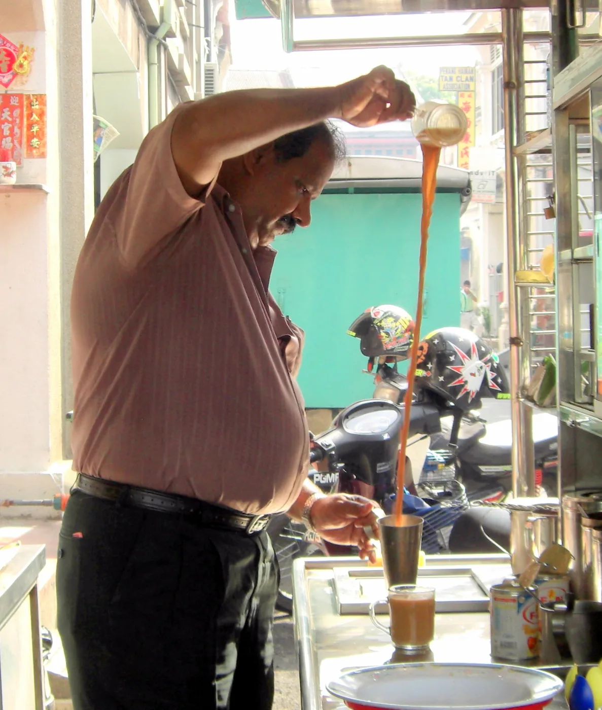 Man pouring tea from a raised mug into another in a long stream