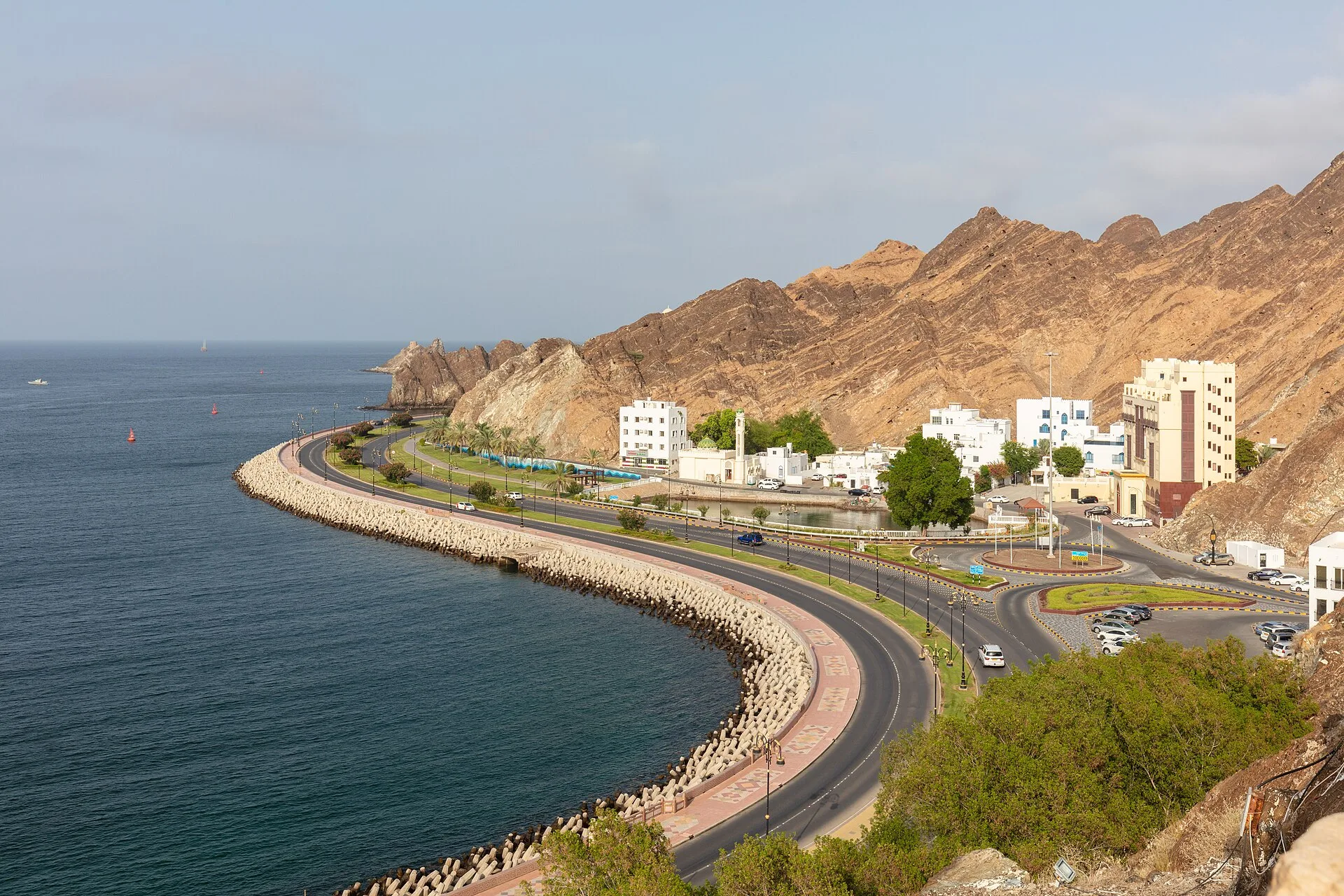 Curving seafront road with white buildings below rocky hills