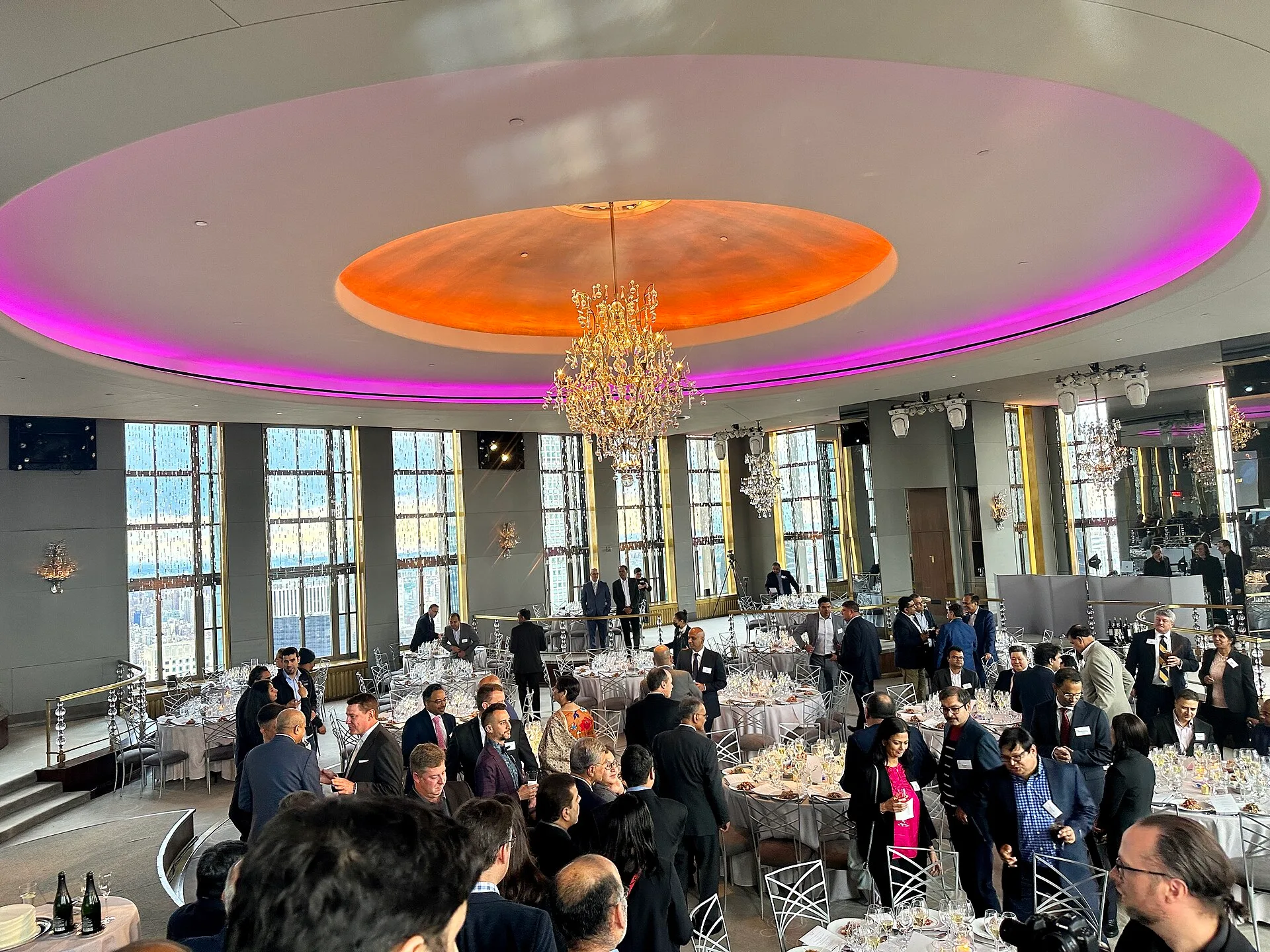 Guests beneath a lit circular ceiling dome and chandelier in a tall-windowed ballroom