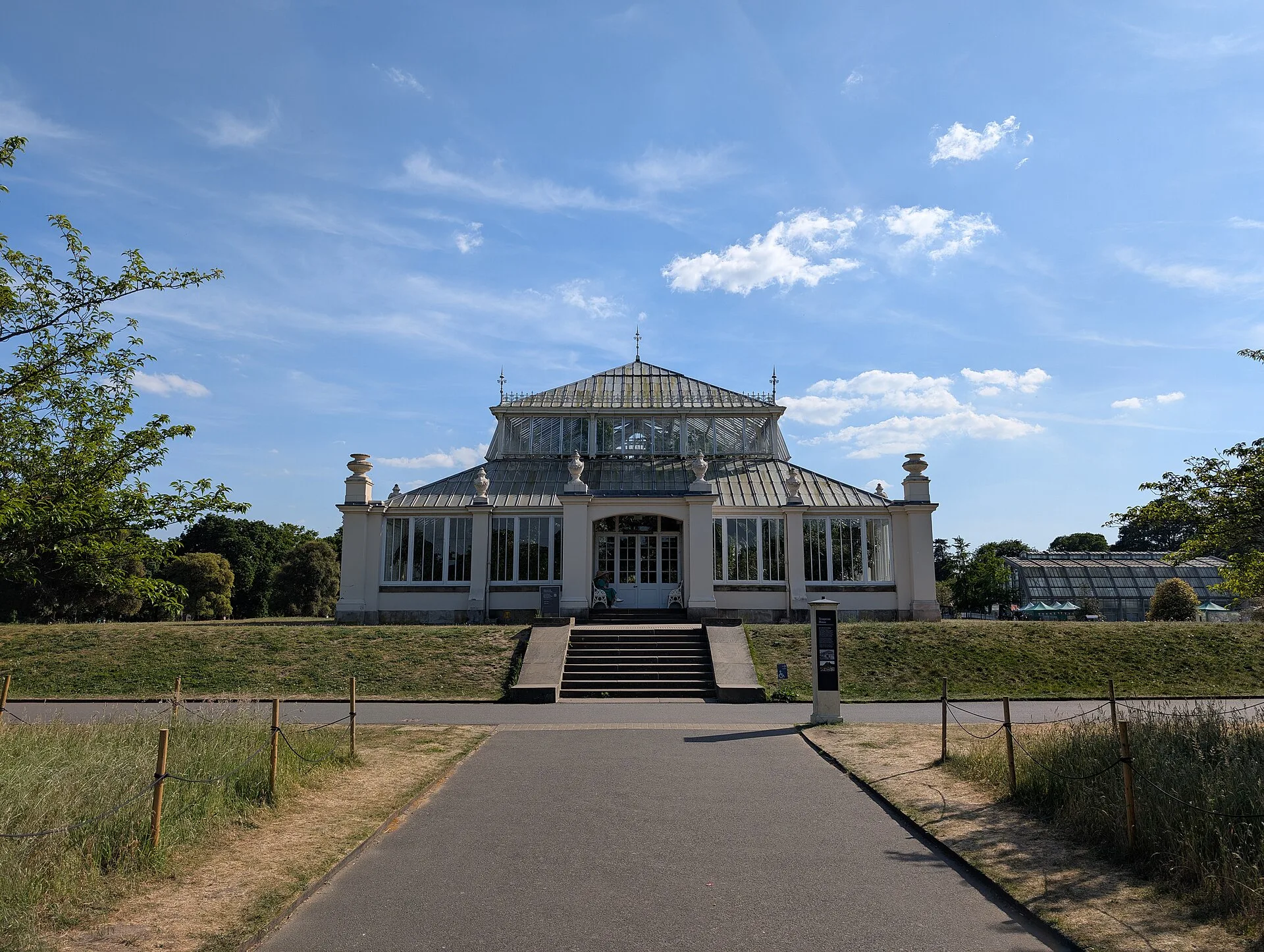 Long white glasshouse with a raised central block at the end of a path