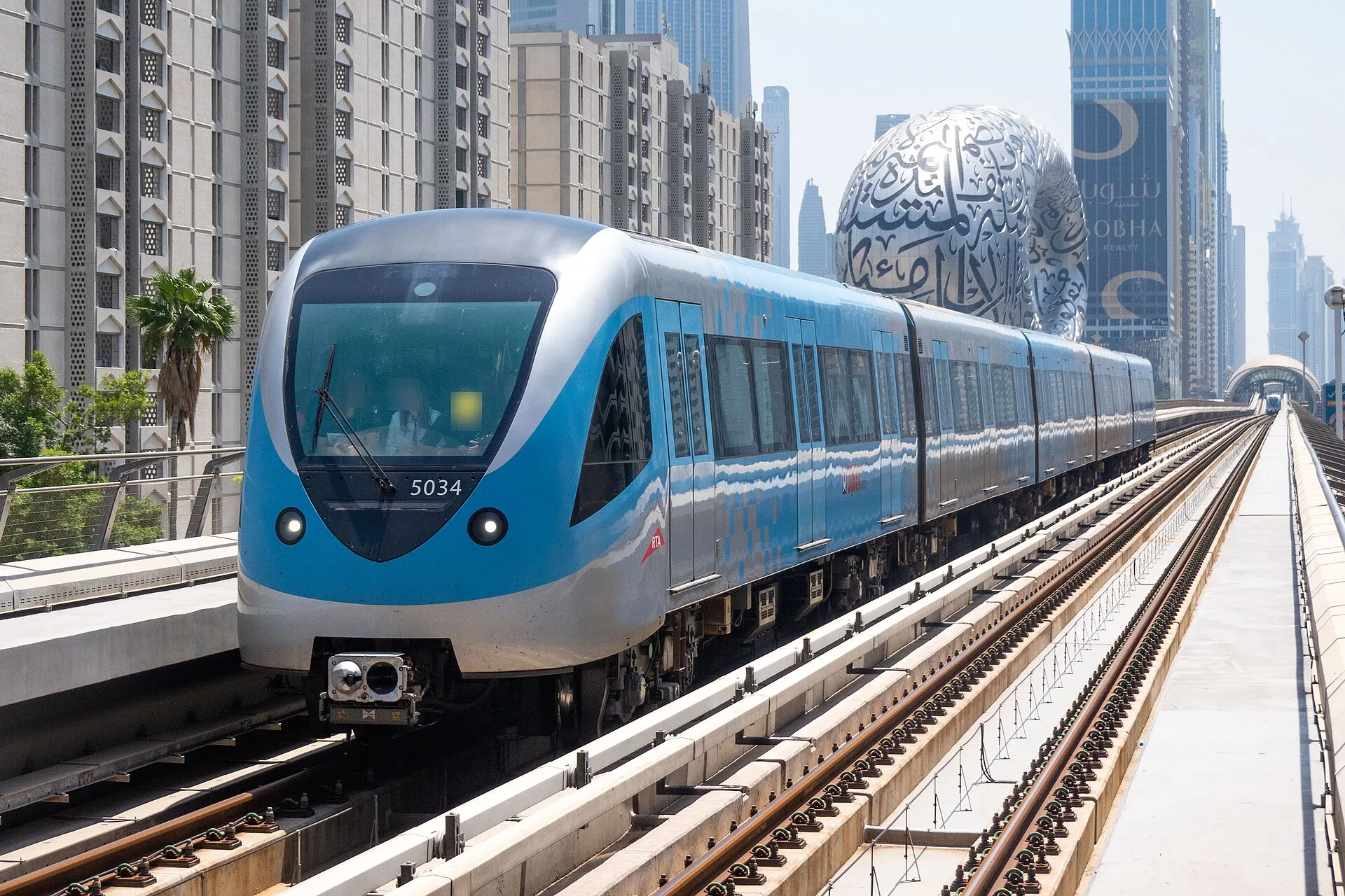 Blue and white metro train on an elevated track entering a station