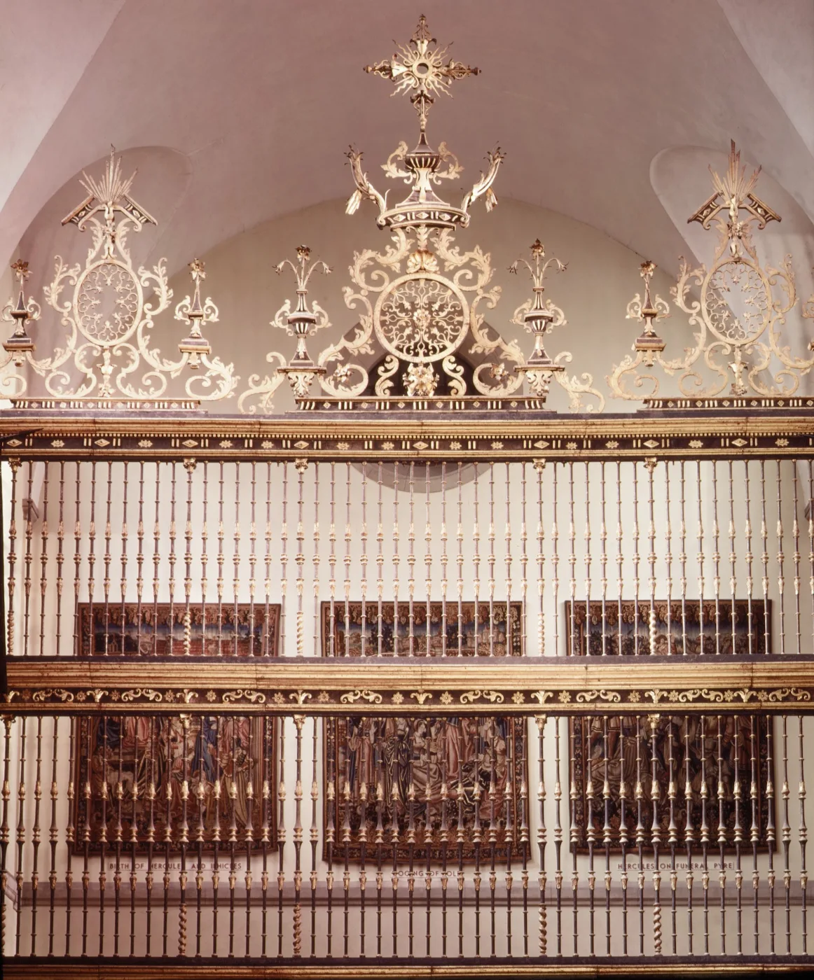 Tall wrought iron choir screen with gilded cresting displayed in a museum hall