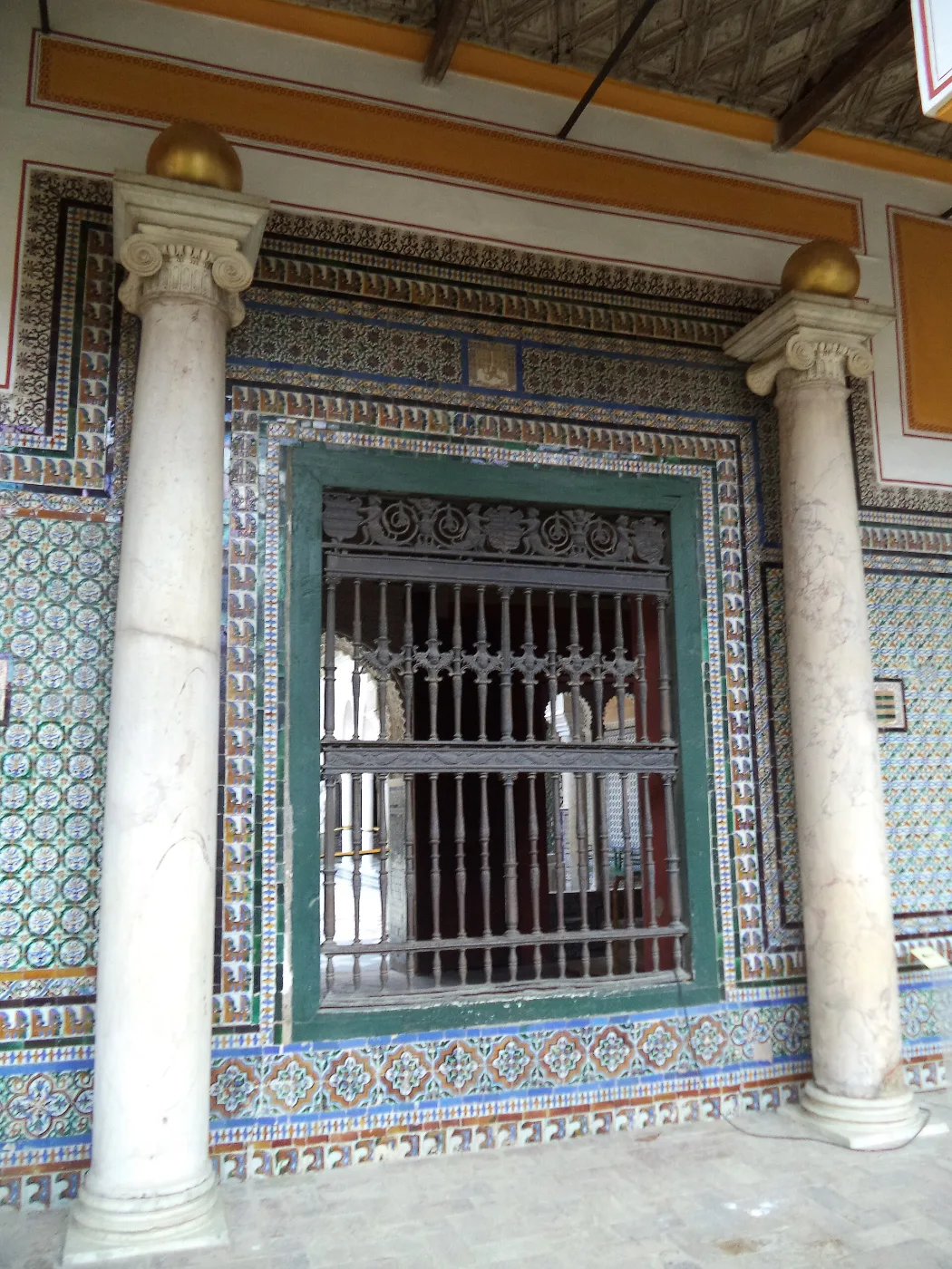 Iron grille over a window framed by tiled walls and marble columns