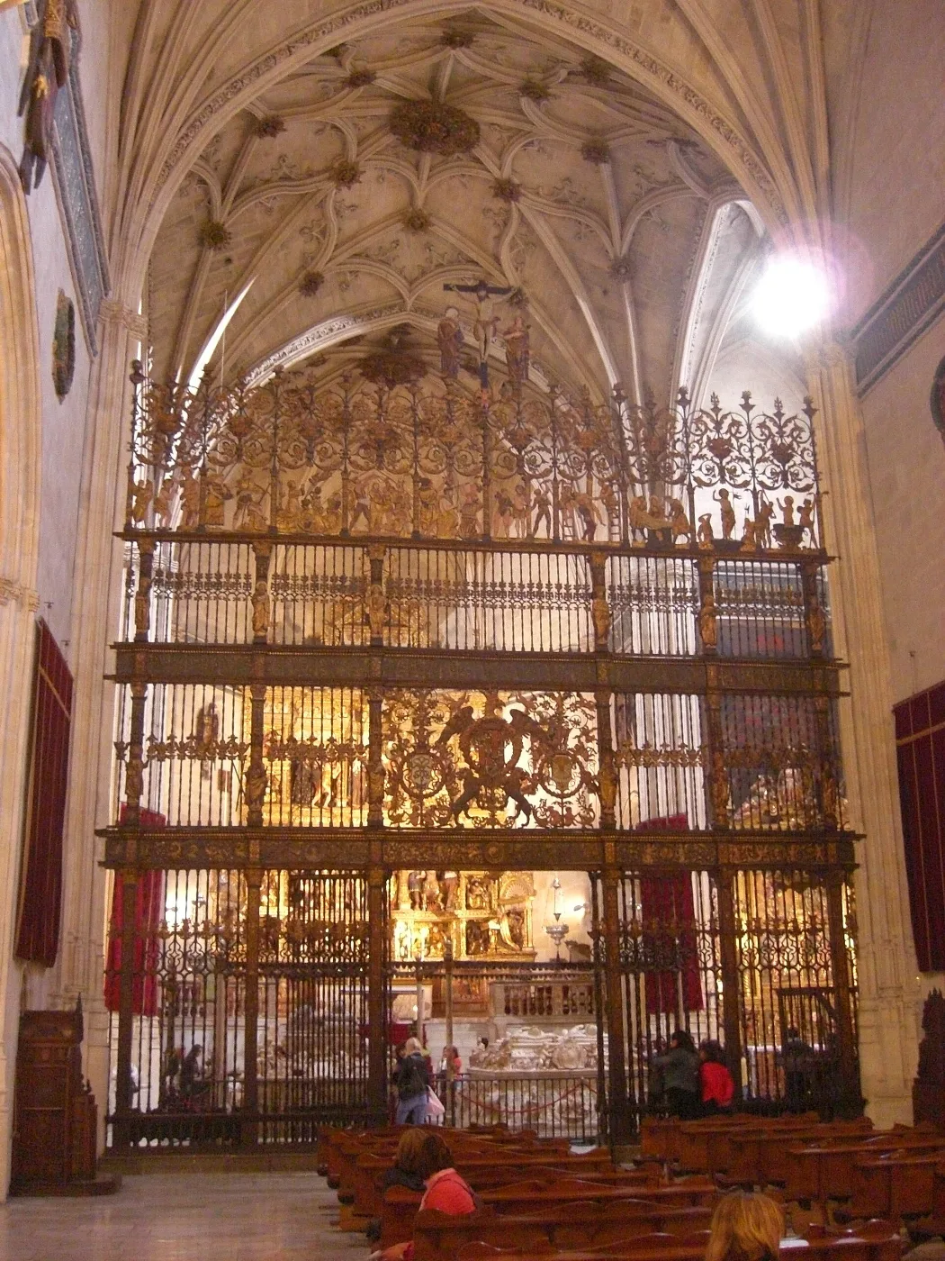 Gilded iron grille spanning a Gothic chapel beneath a ribbed vault