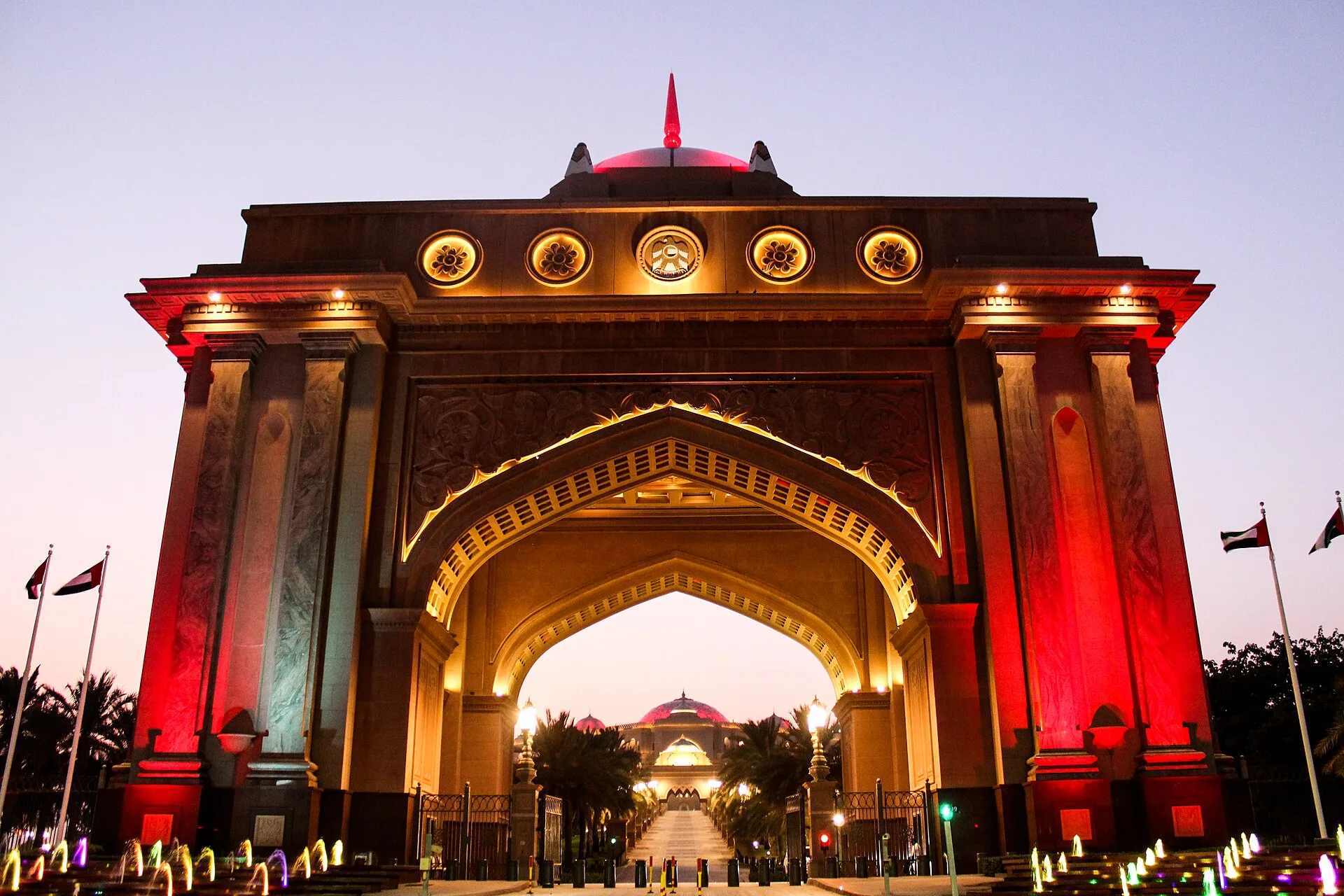 Illuminated arched gateway of Emirates Palace glowing red and gold at night