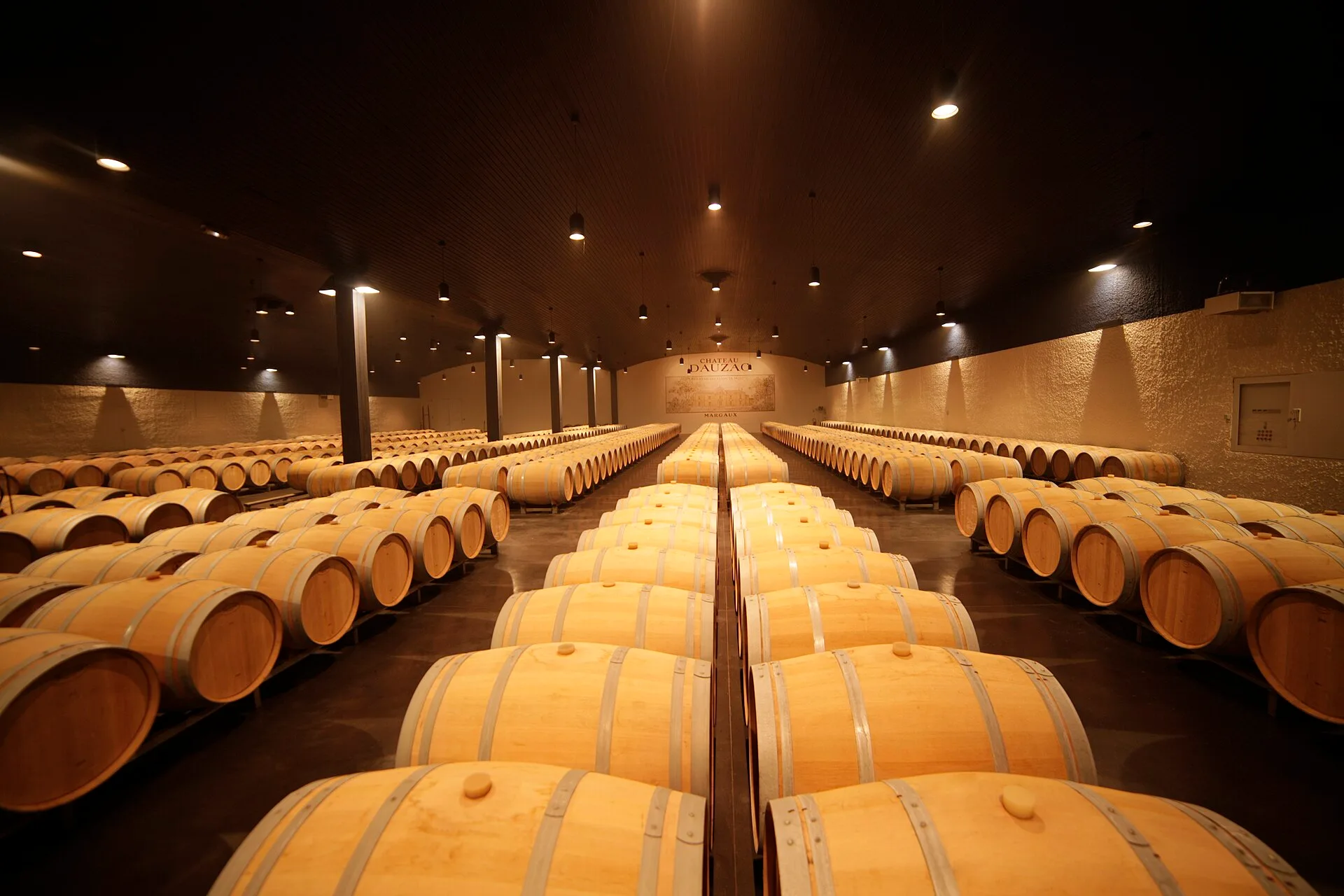 Long rows of oak wine barrels on racks in a dimly lit barrel hall