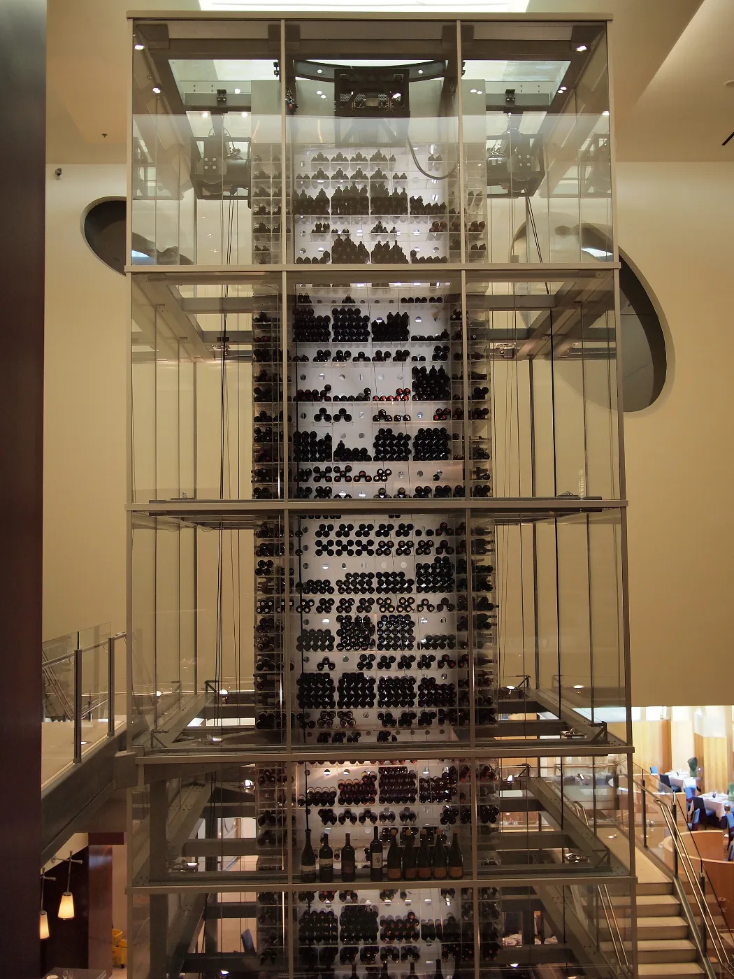Tall illuminated glass wine tower filled with racked bottles inside a restaurant