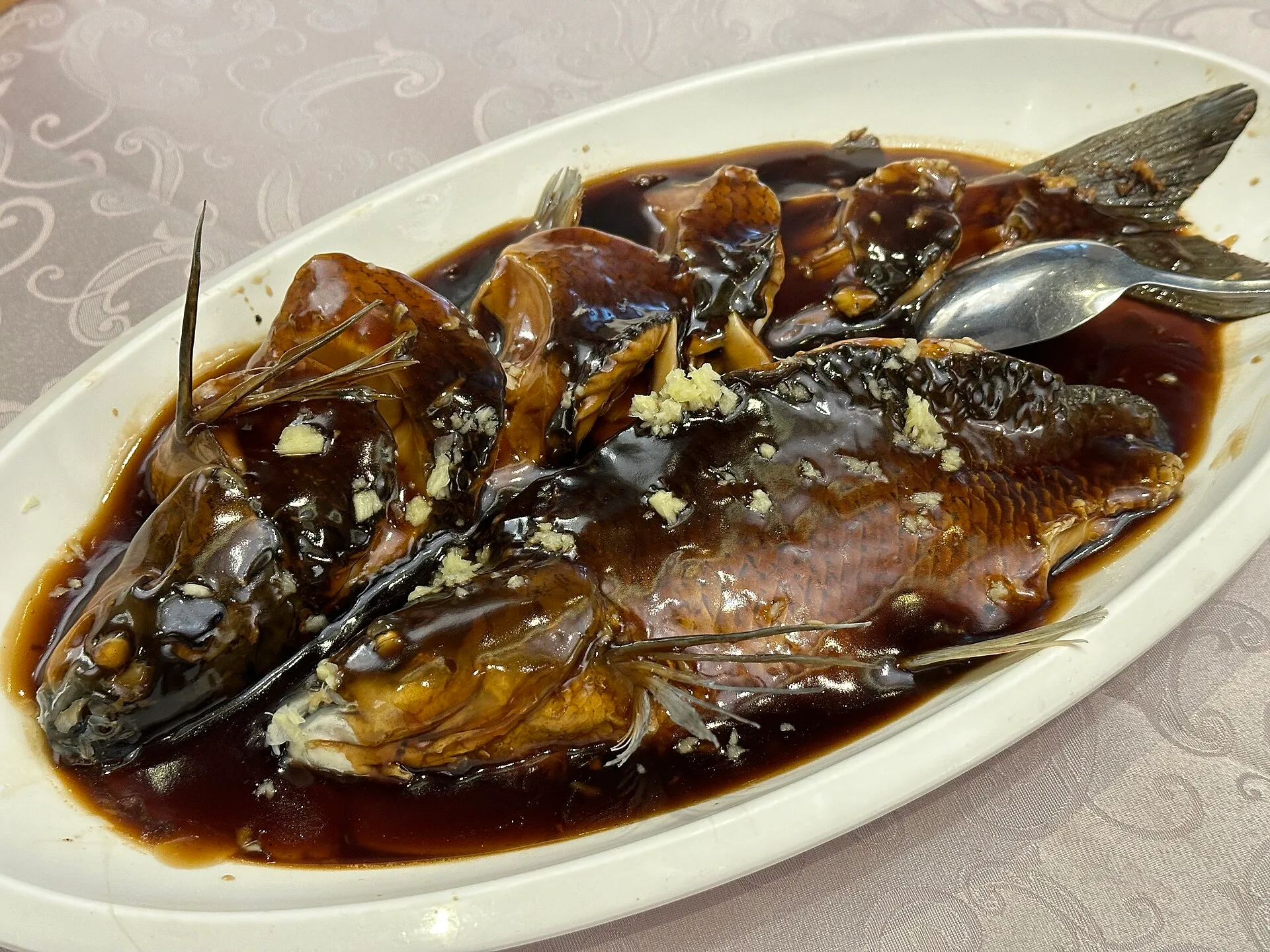 Whole fish on a white plate covered in glossy brown vinegar sauce