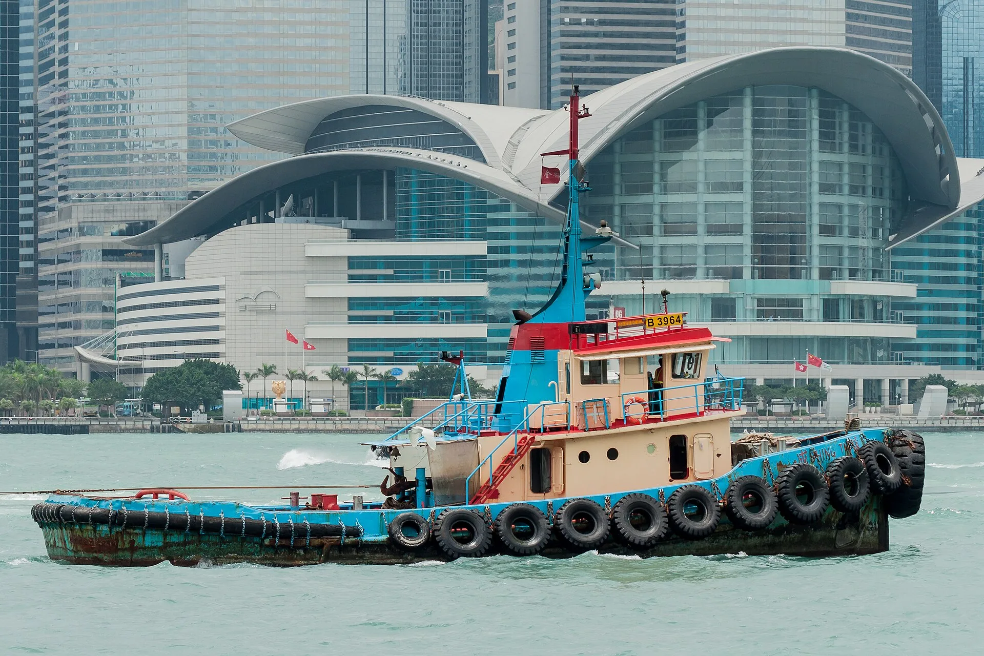 Red towboat on the harbour in front of a curved glass convention centre