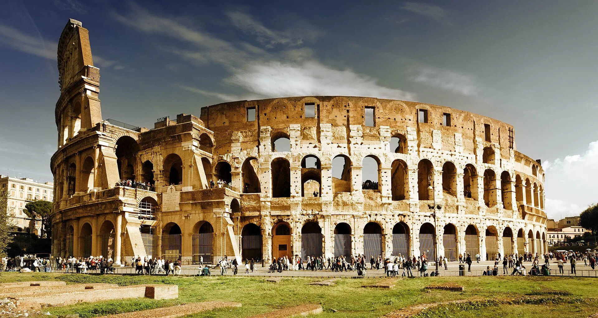 Tiered stone arcades of a ruined Roman amphitheatre with visitors at its base