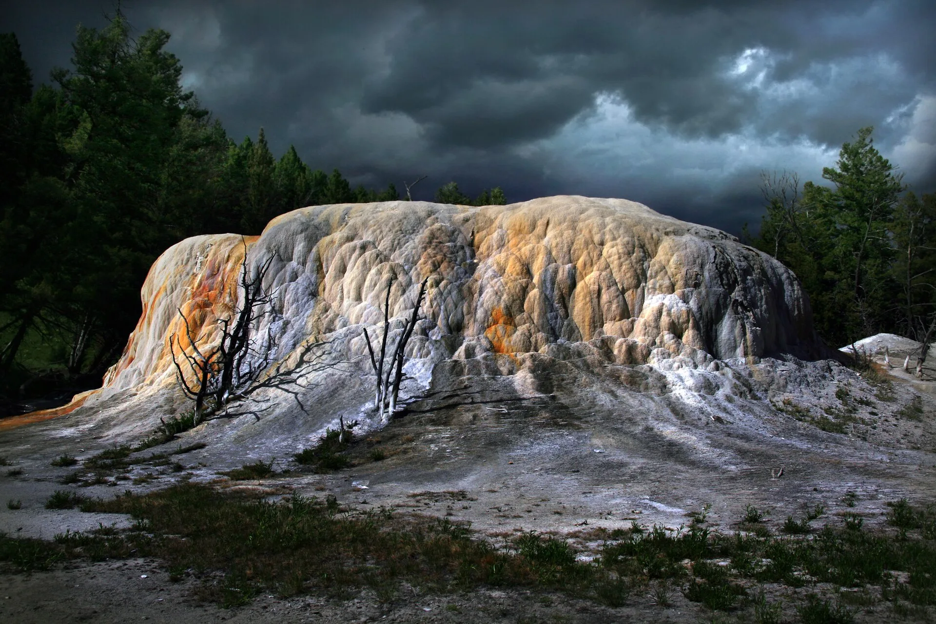 Rounded mineral mound streaked orange and white beneath dark clouds