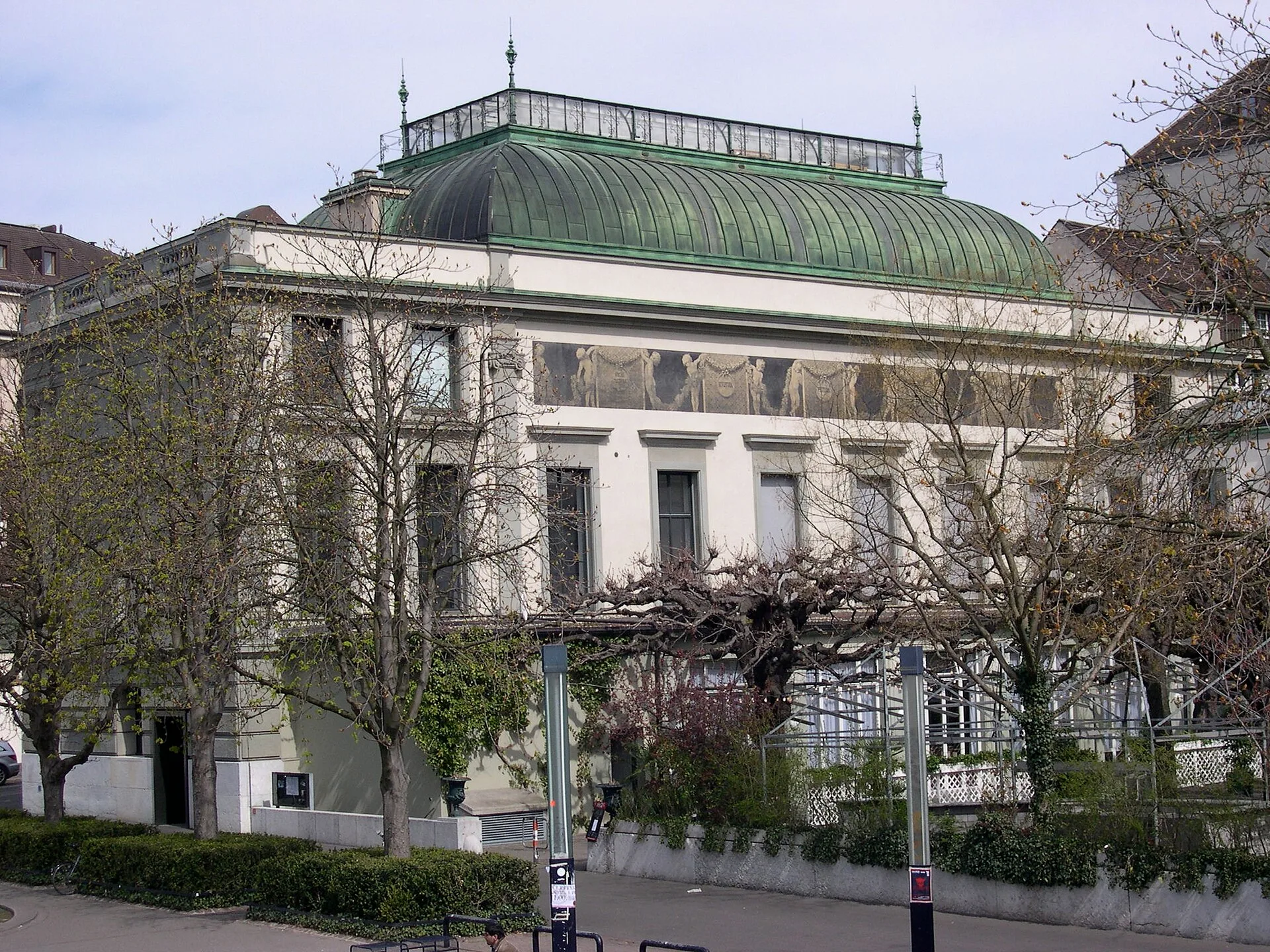 Stone gallery building with a green copper roof behind bare trees