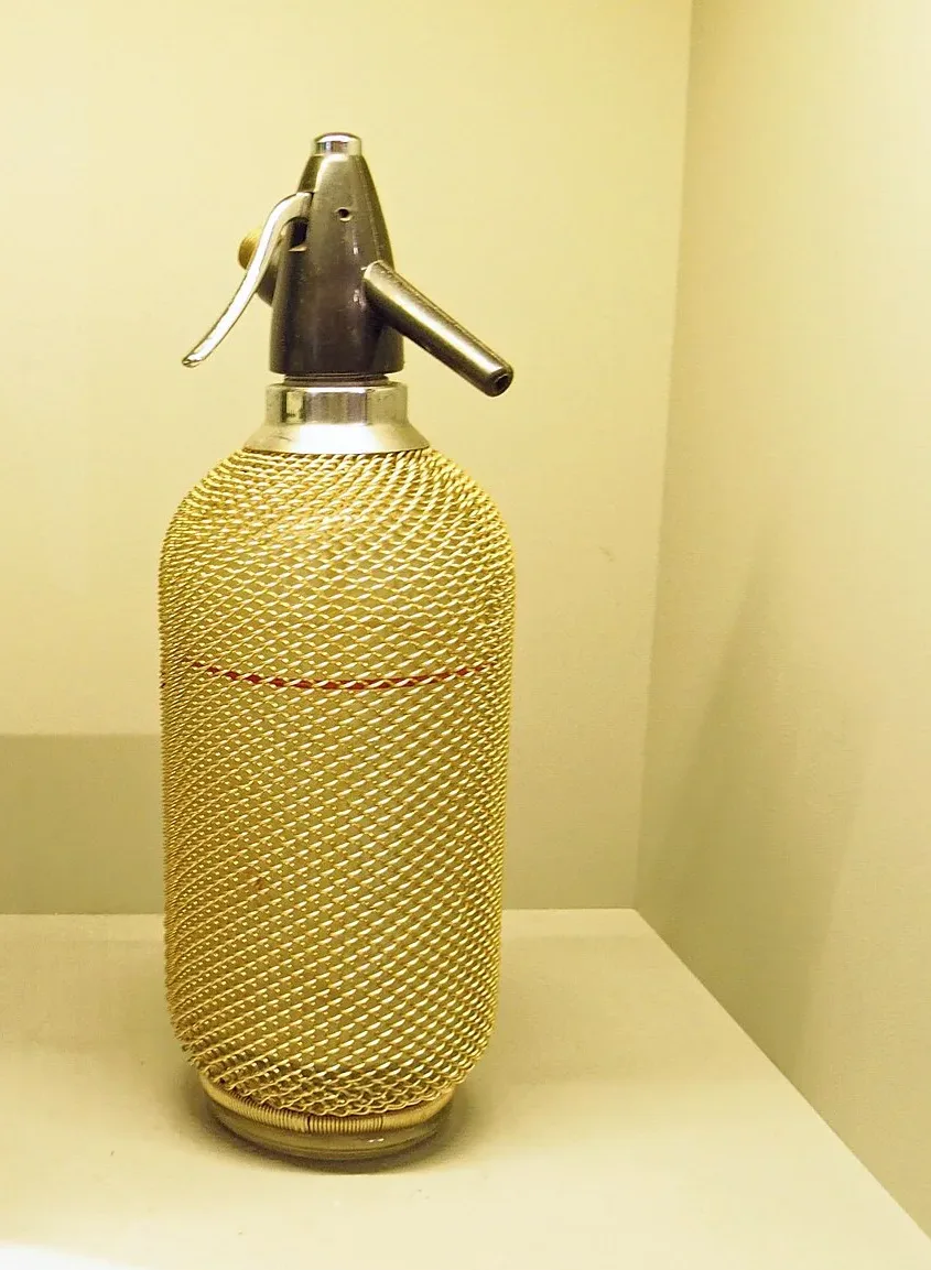 Glass soda siphon bottle wrapped in wire mesh with a metal head