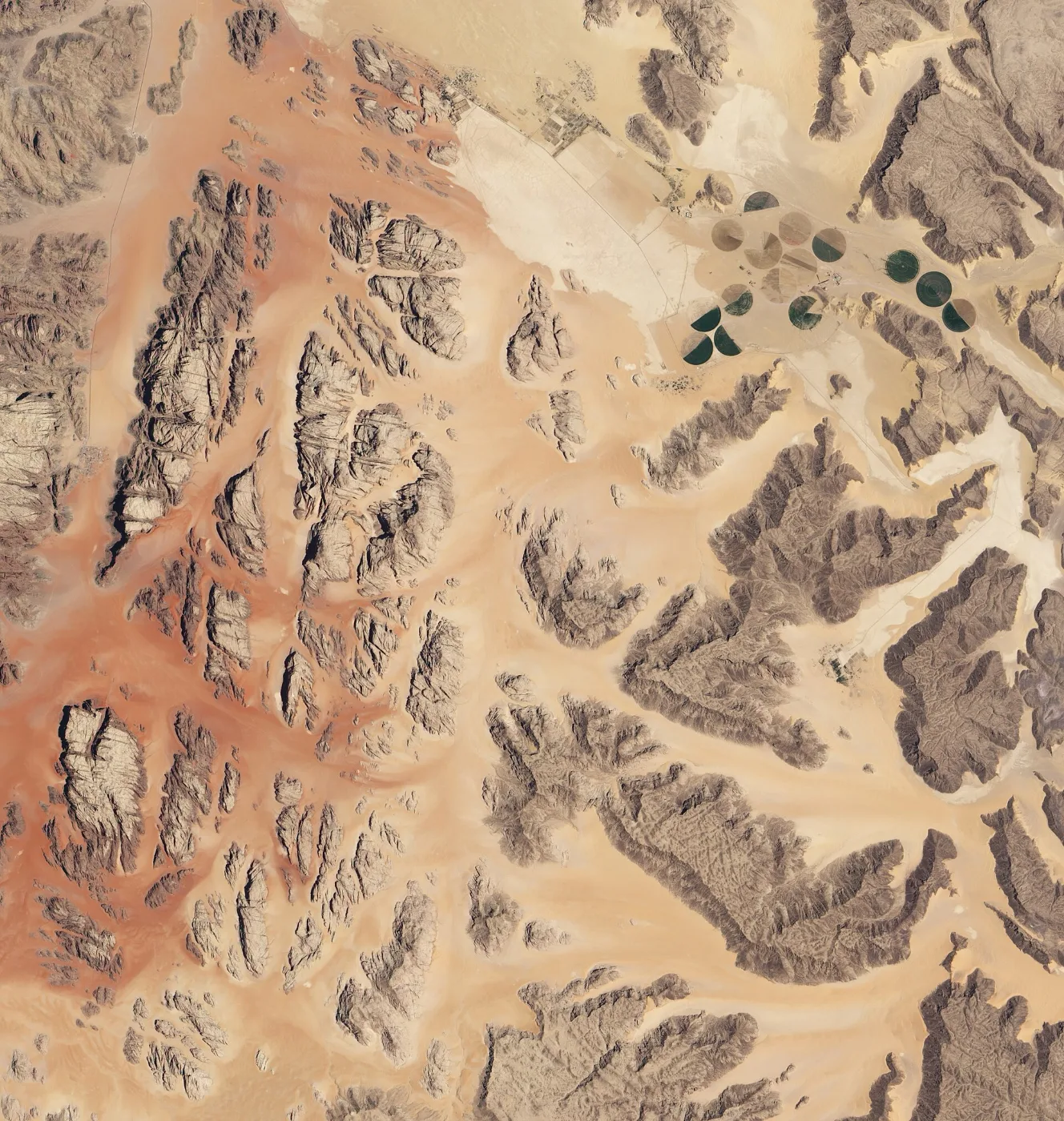 Satellite view of dark rock massifs separated by pale sandy valleys