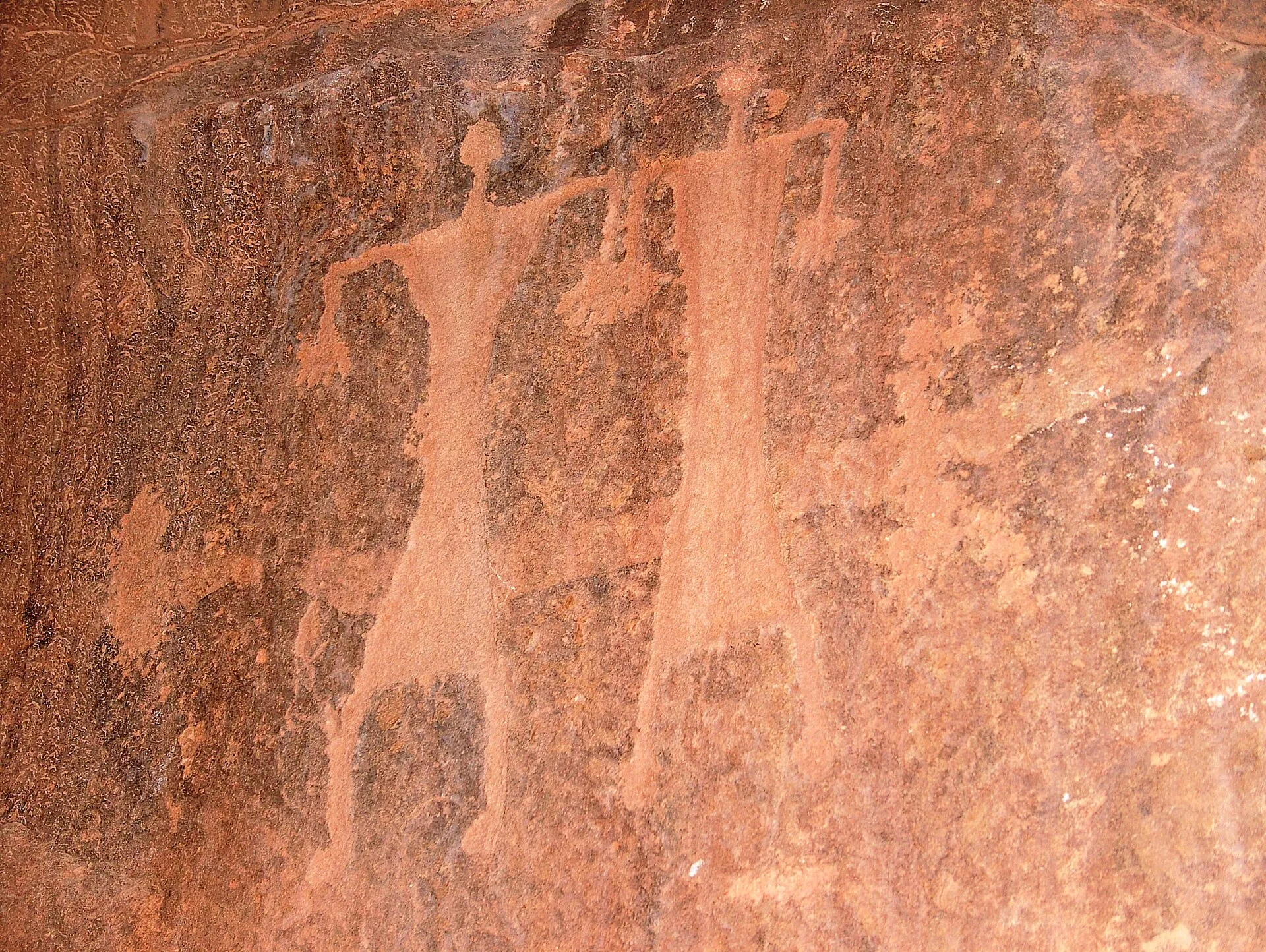 Human figures pecked into a reddish sandstone rock face