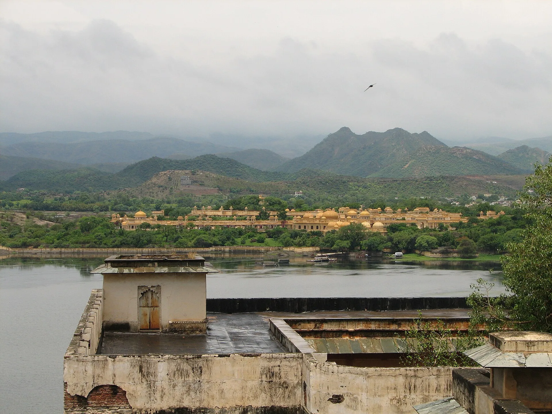 Sandstone resort rooftops beside a lake with green hills beyond