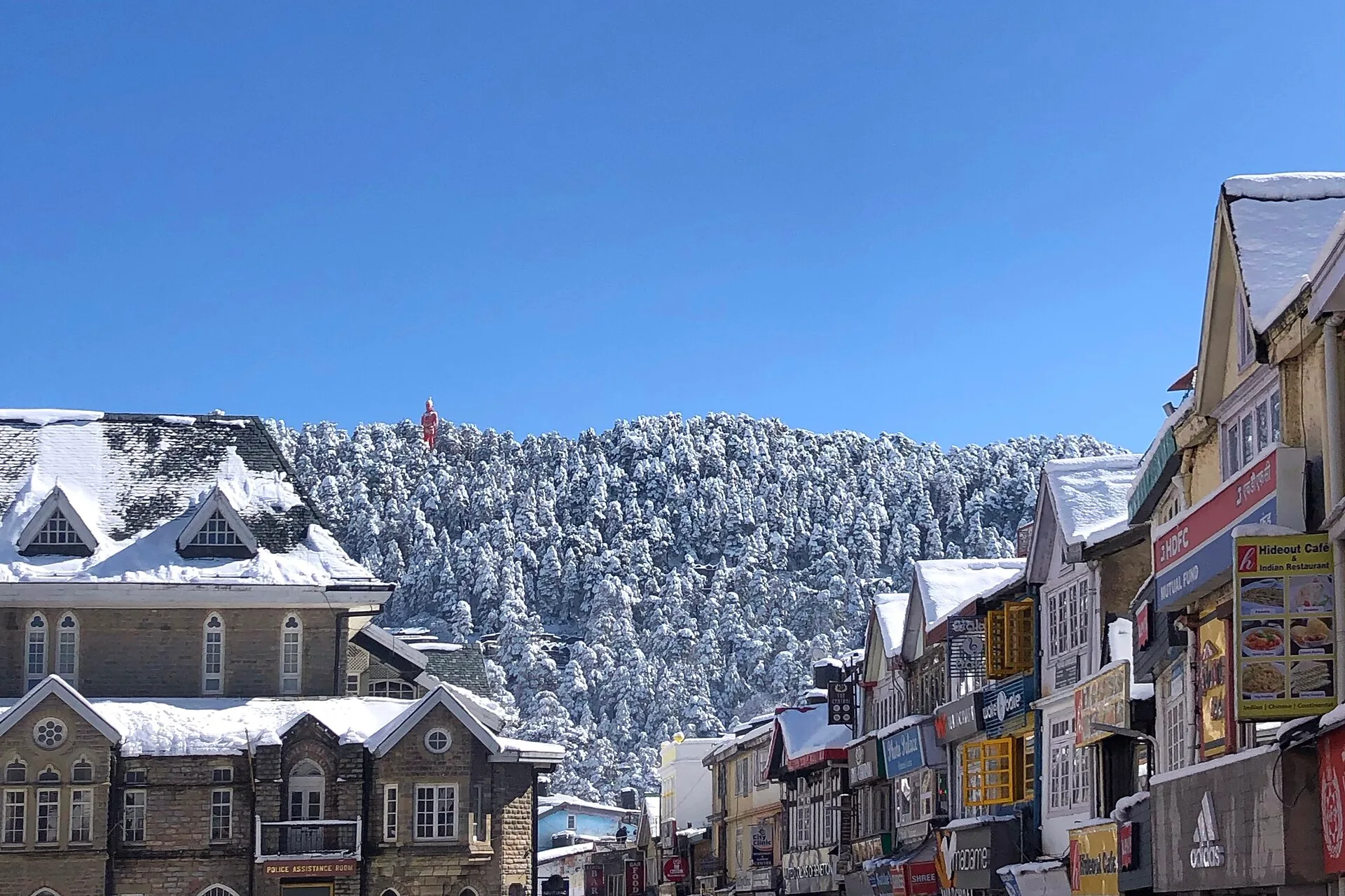 Snow-covered rooftops along a hill town street below a forested ridge