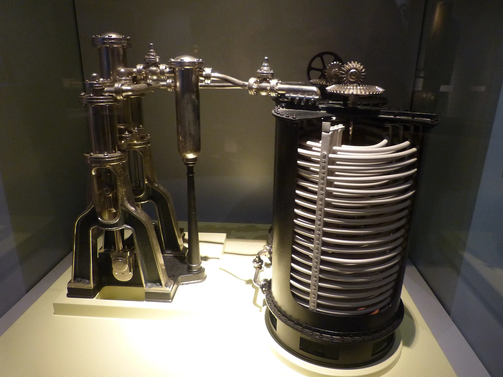 Black metal compressor model with a coiled cylinder in a glass display case