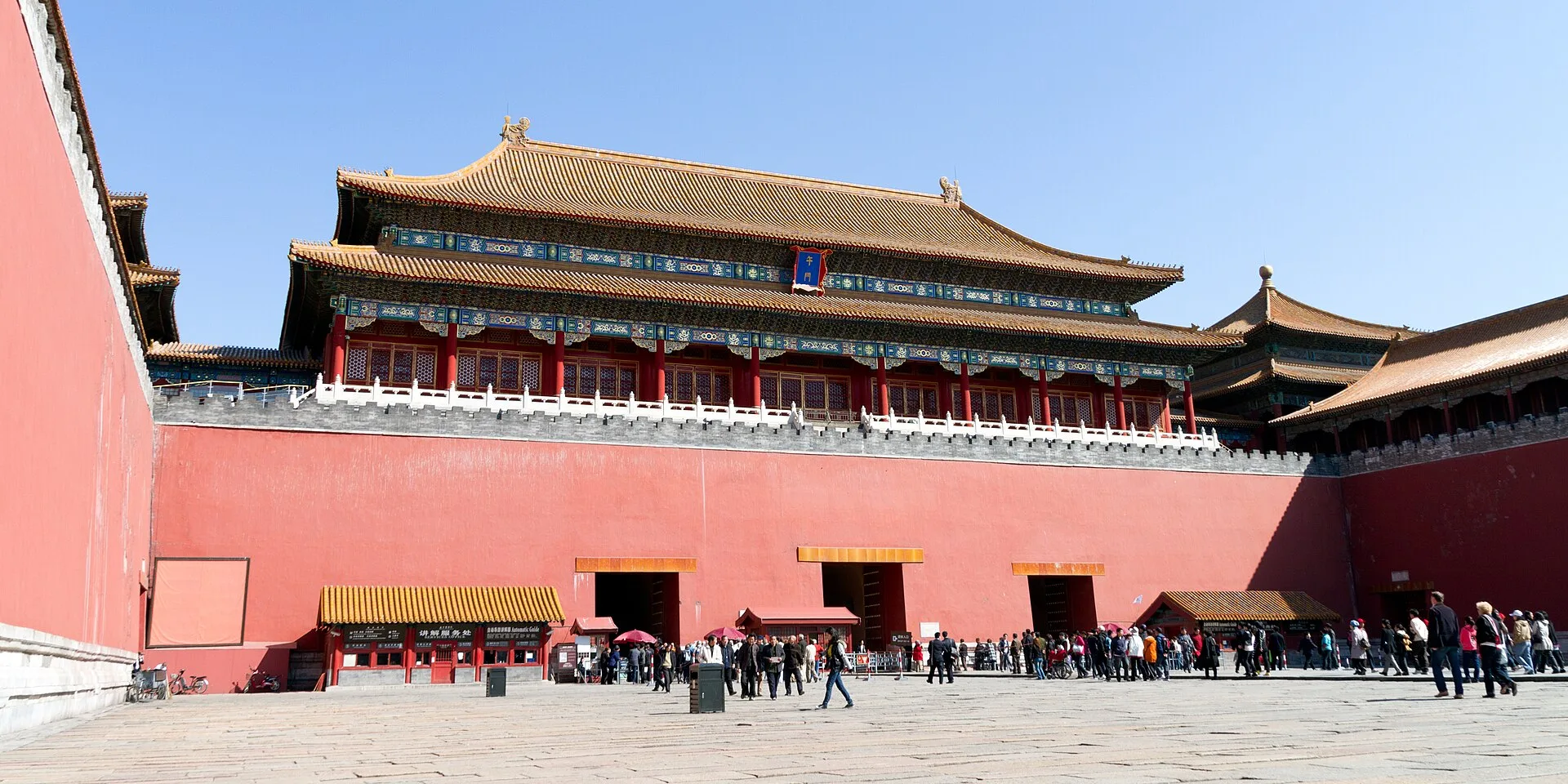 Red walled gatehouse with yellow roofed pavilions above a wide paved courtyard