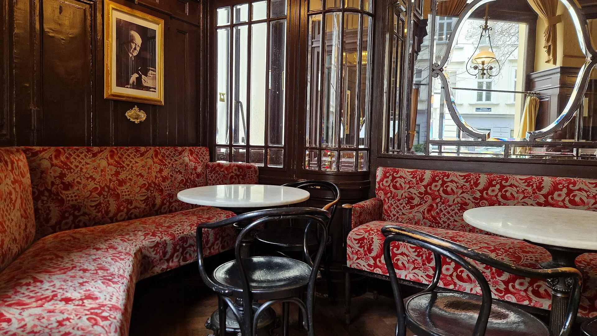 Red upholstered banquettes, marble tables and bentwood chairs in a panelled café