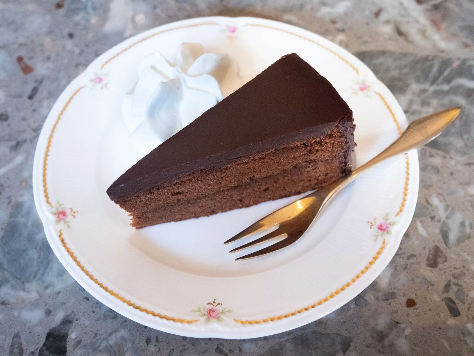Slice of chocolate cake with whipped cream and a fork on a white plate