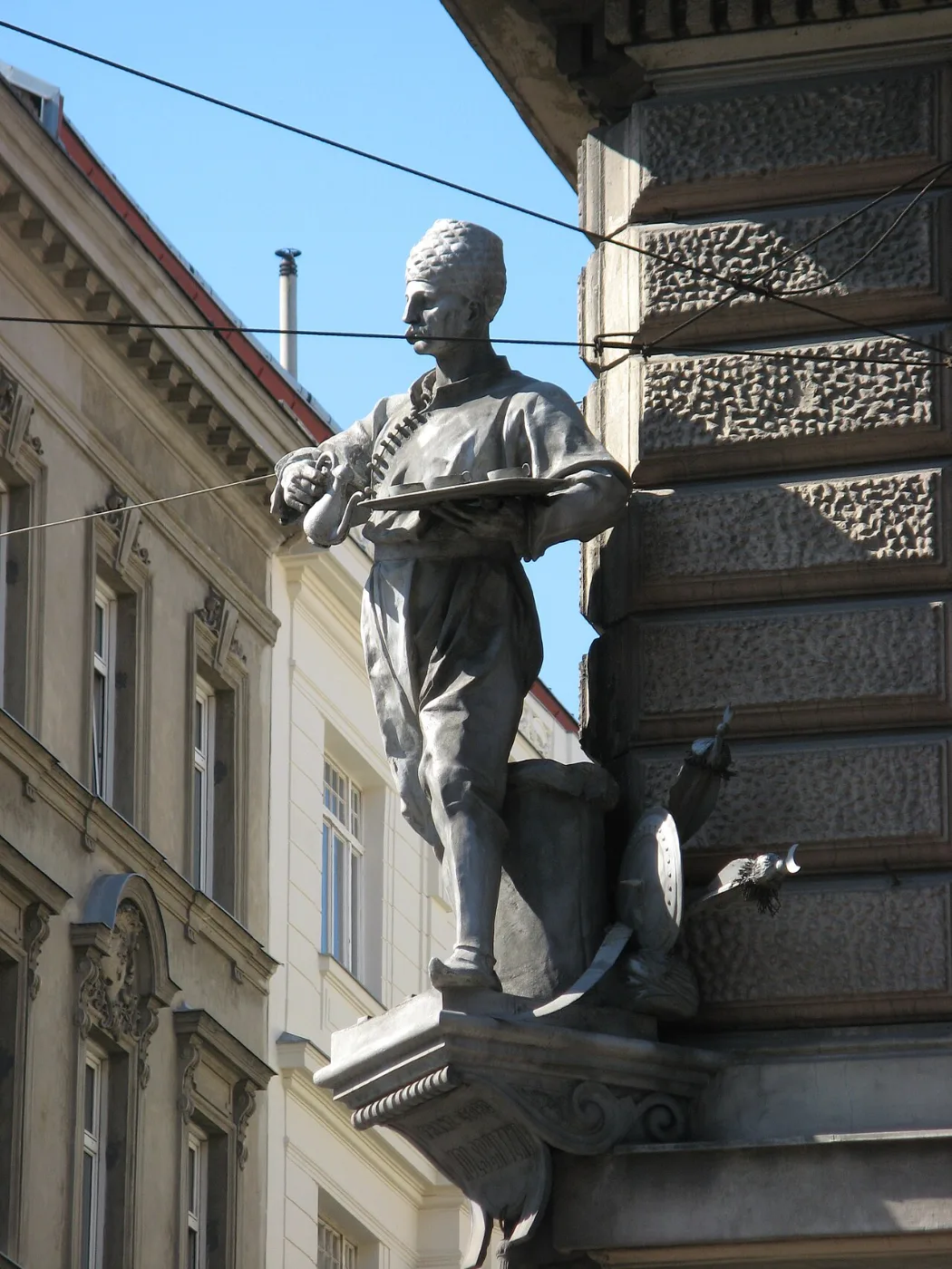 Bronze statue of a man holding a tray mounted on a building corner