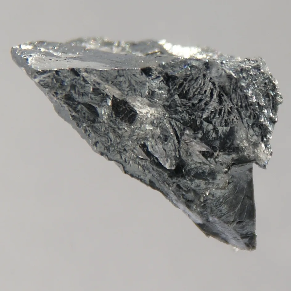 Shiny silvery piece of chromium metal on a grey background