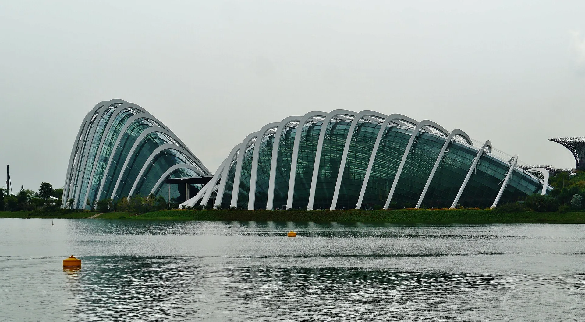 Two ribbed glass conservatory domes on a waterfront under an overcast sky