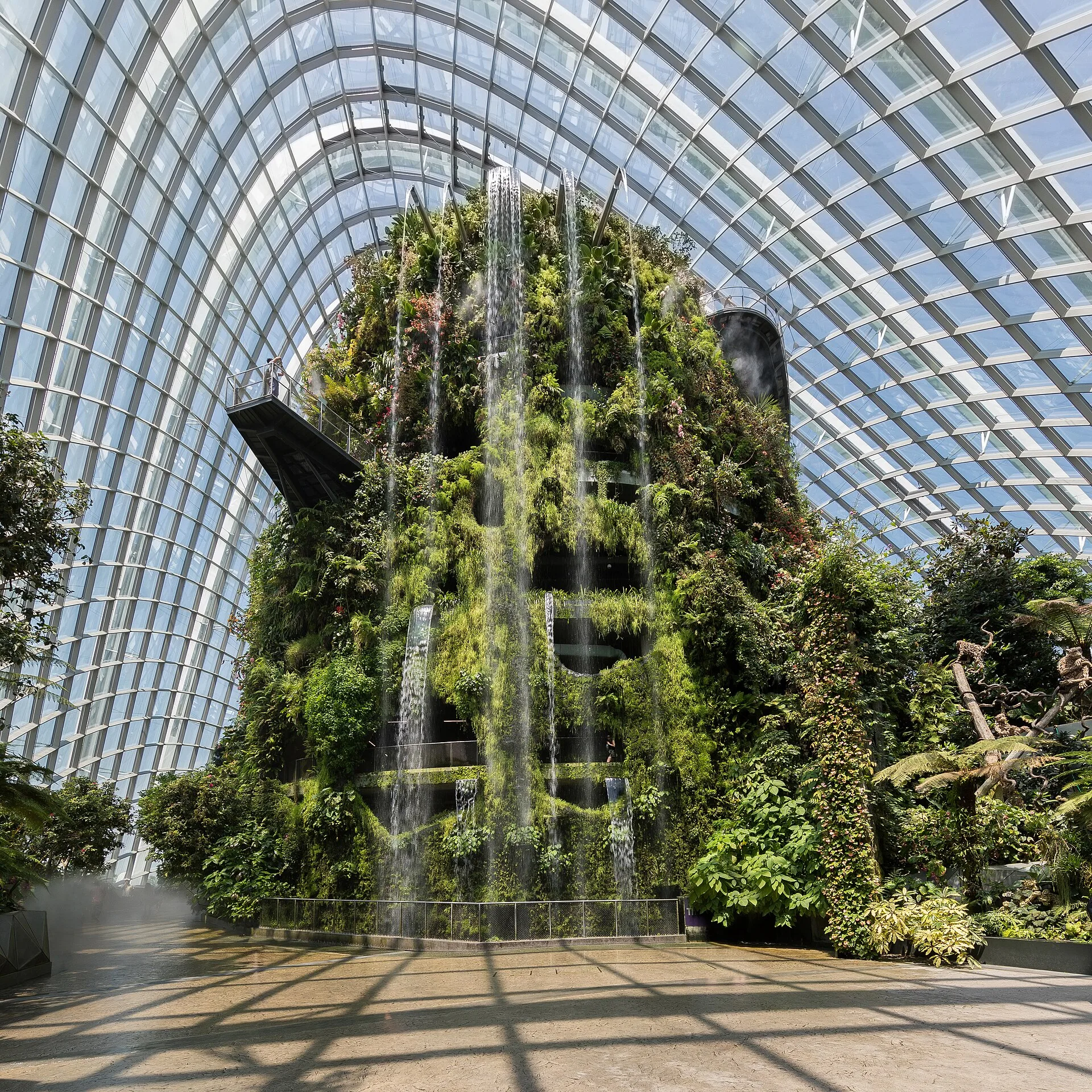Plant-covered artificial mountain with a waterfall inside a glass conservatory