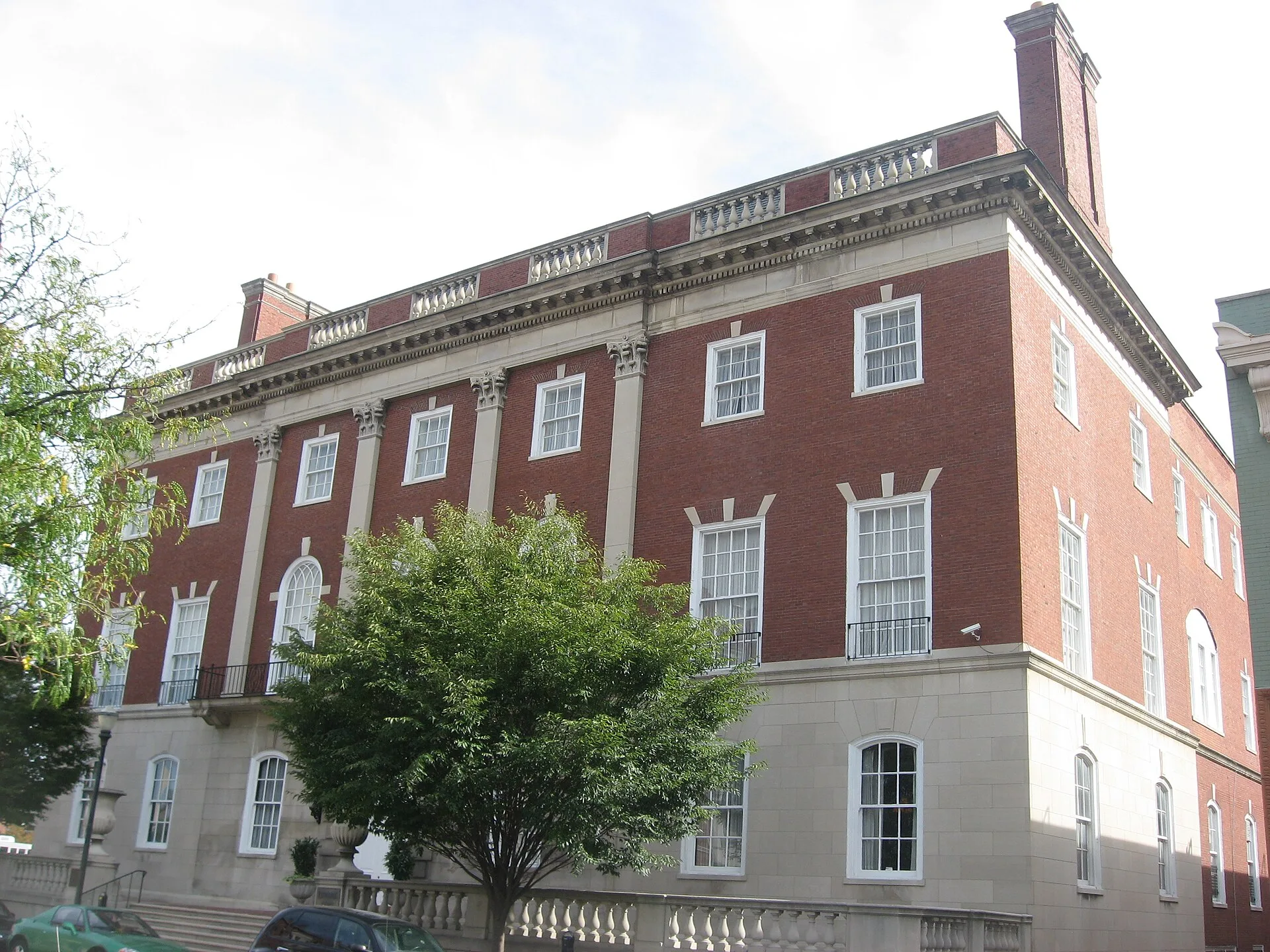 Red brick neoclassical clubhouse with tall windows behind a tree