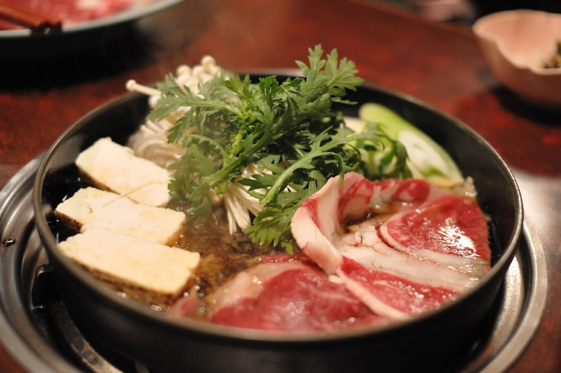 Iron pot of sukiyaki with sliced beef, tofu and vegetables