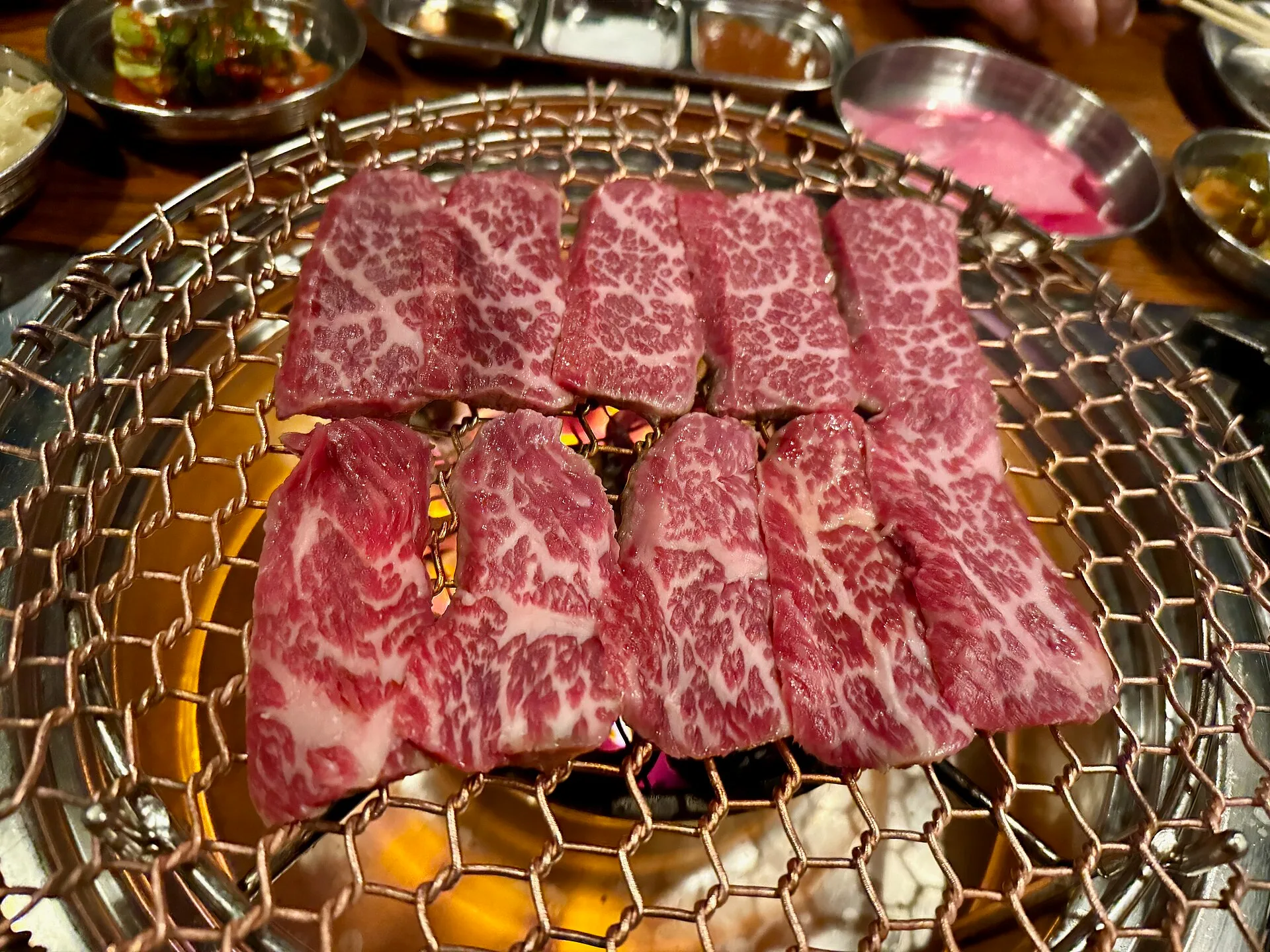 Slices of heavily marbled raw beef laid on a round tabletop grill