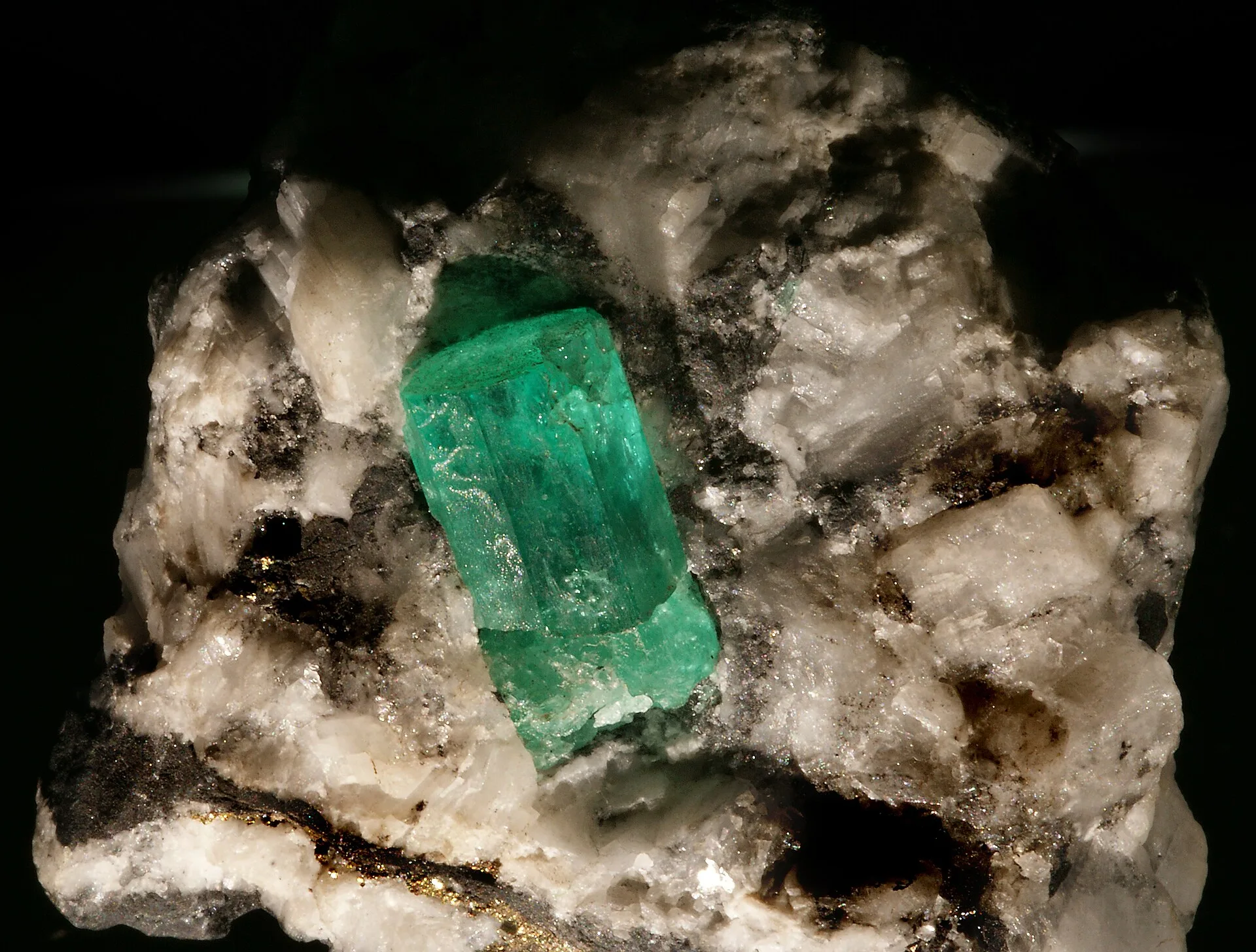 Green emerald crystal embedded in white and dark mineral rock