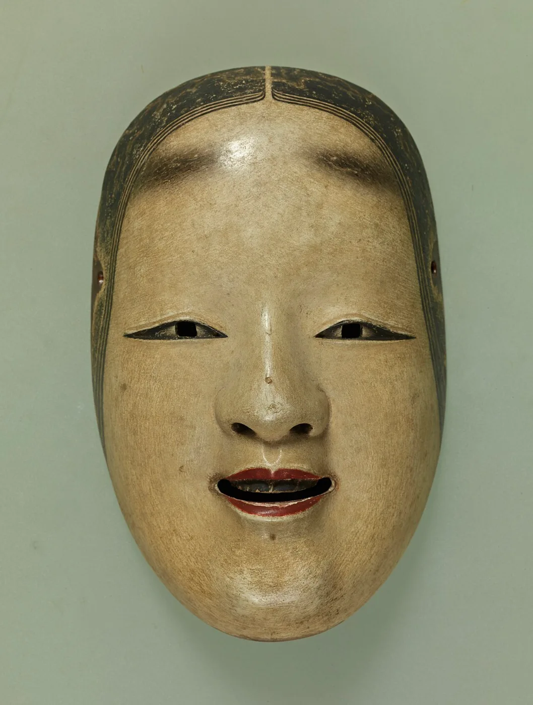Carved white mask of a young woman's face with painted eyebrows