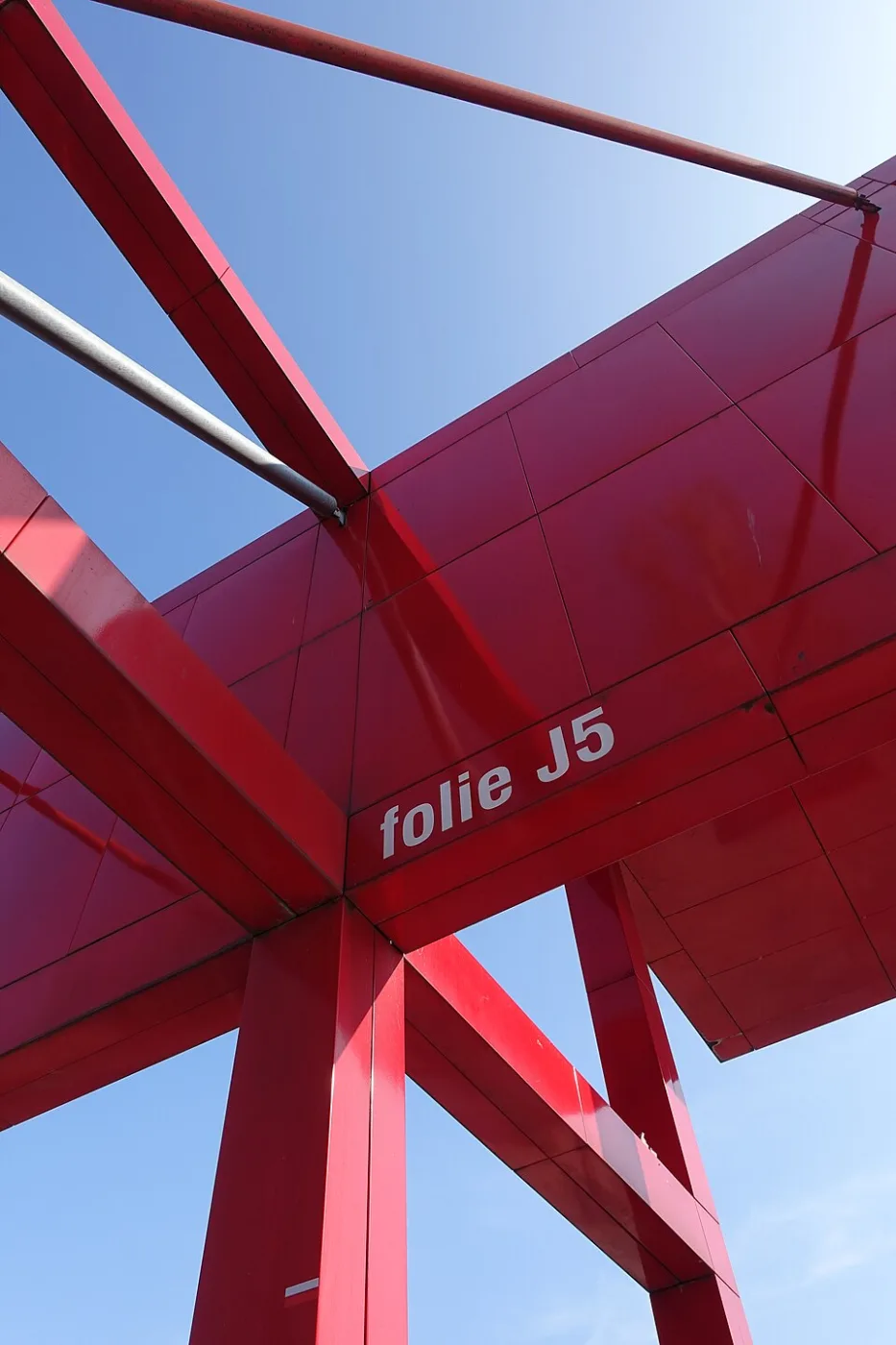 Bright red steel frame structure seen from below against a blue sky