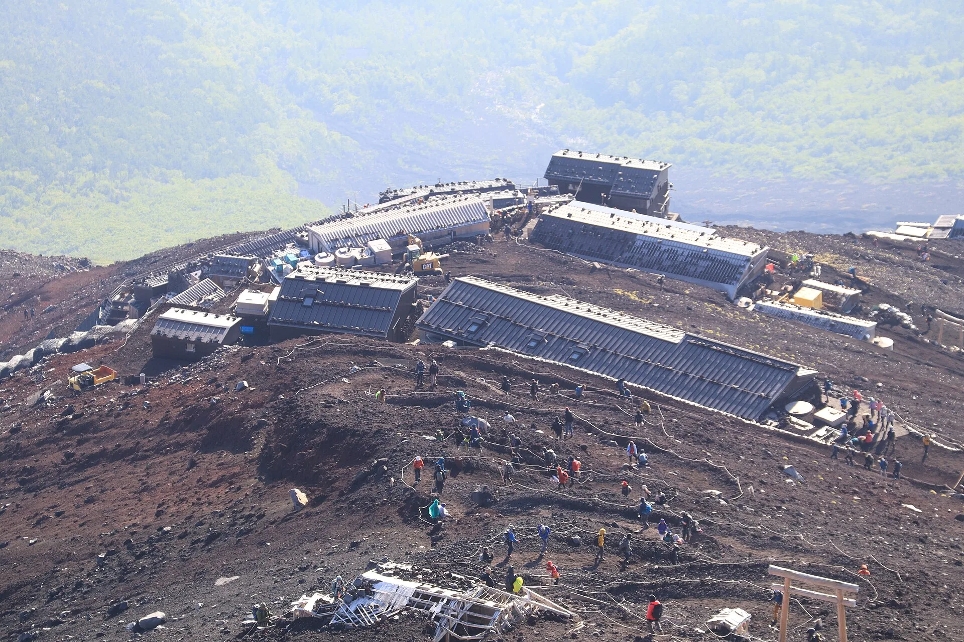 Mountain huts and climbers on a bare volcanic slope above the clouds