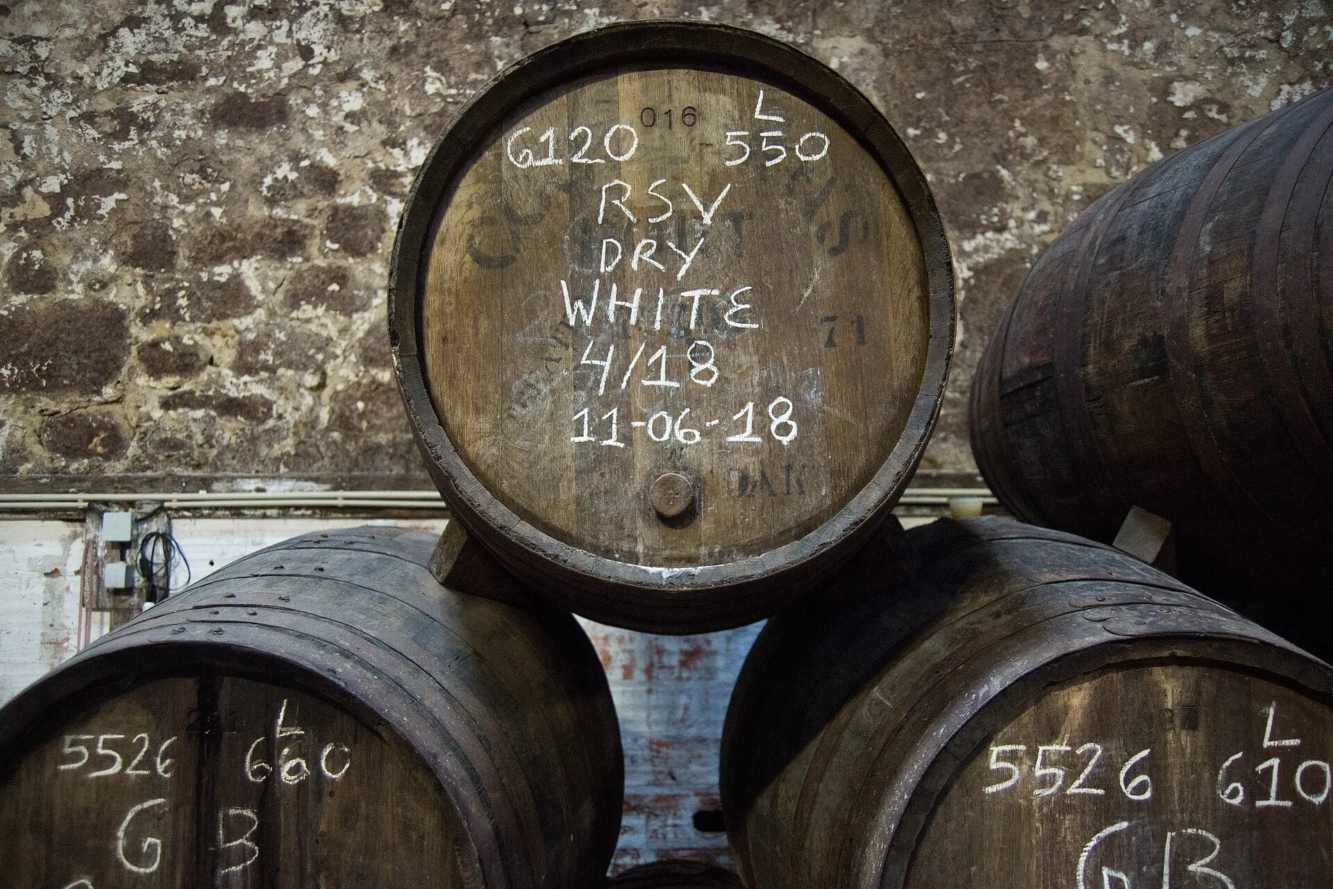 Stacked oak casks with chalk markings in a stone cellar