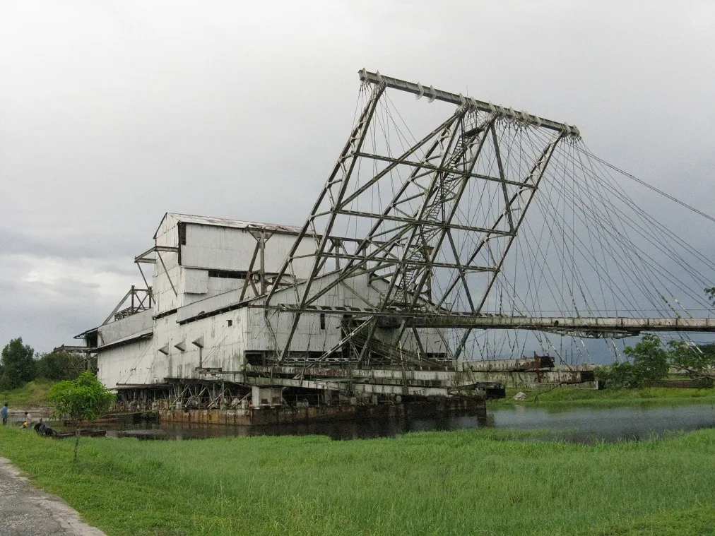 Large steel tin dredge with a tall gantry standing in a grassy field