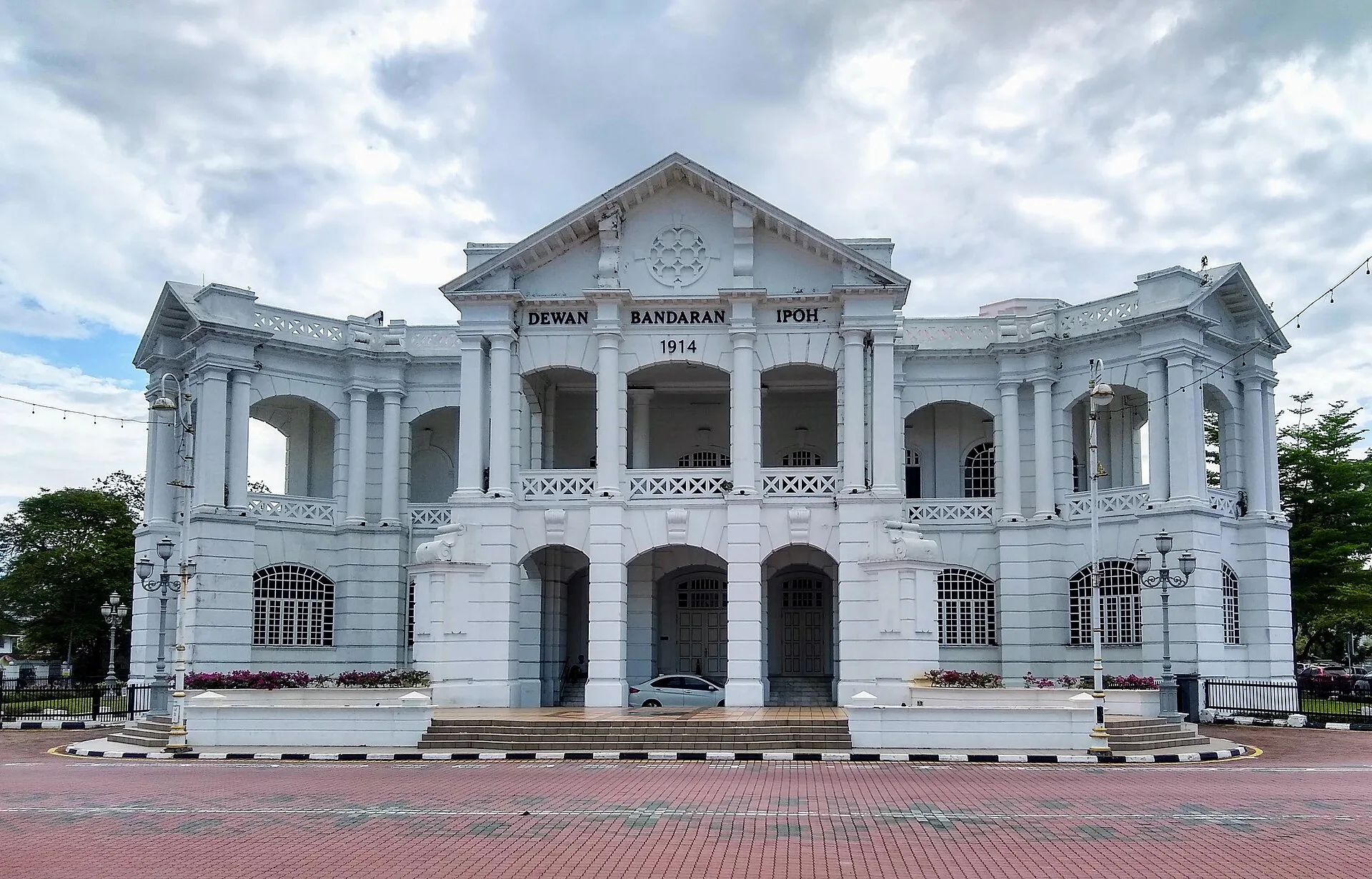 White neoclassical town hall with arched colonnades under a cloudy sky