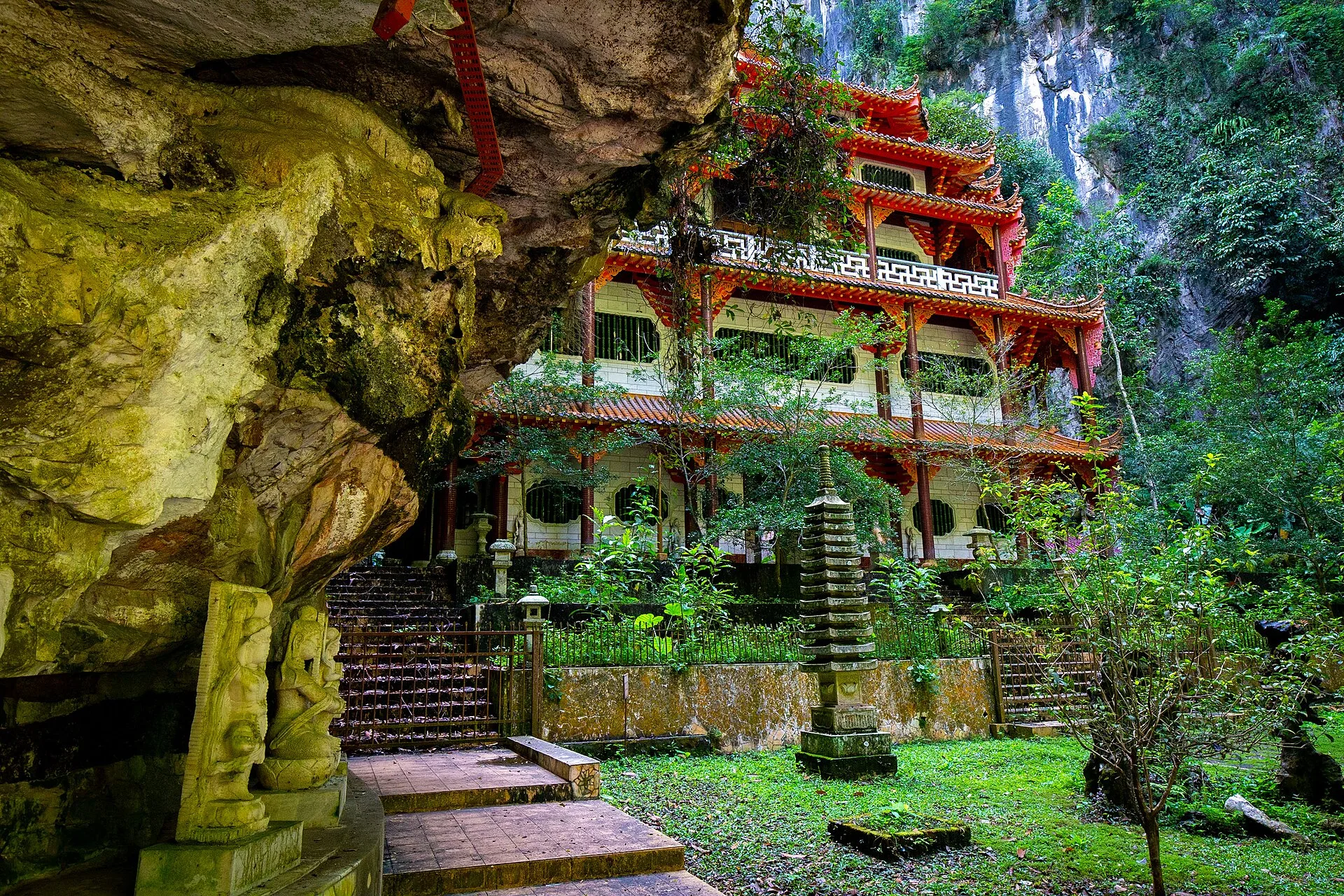 Red and white temple pavilion set against a limestone cliff and greenery