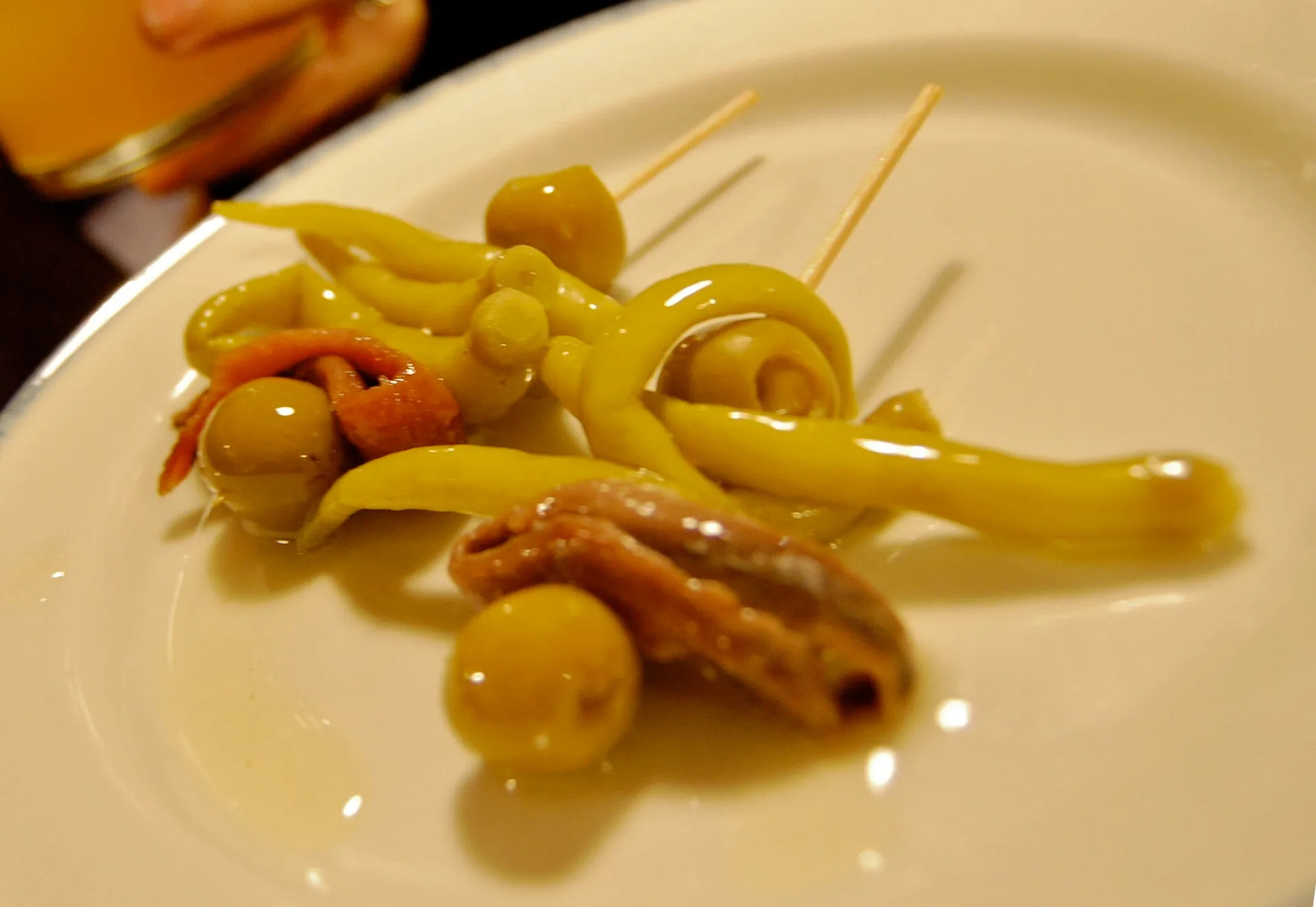 Skewers of green chilli peppers, olives and anchovy on a white plate