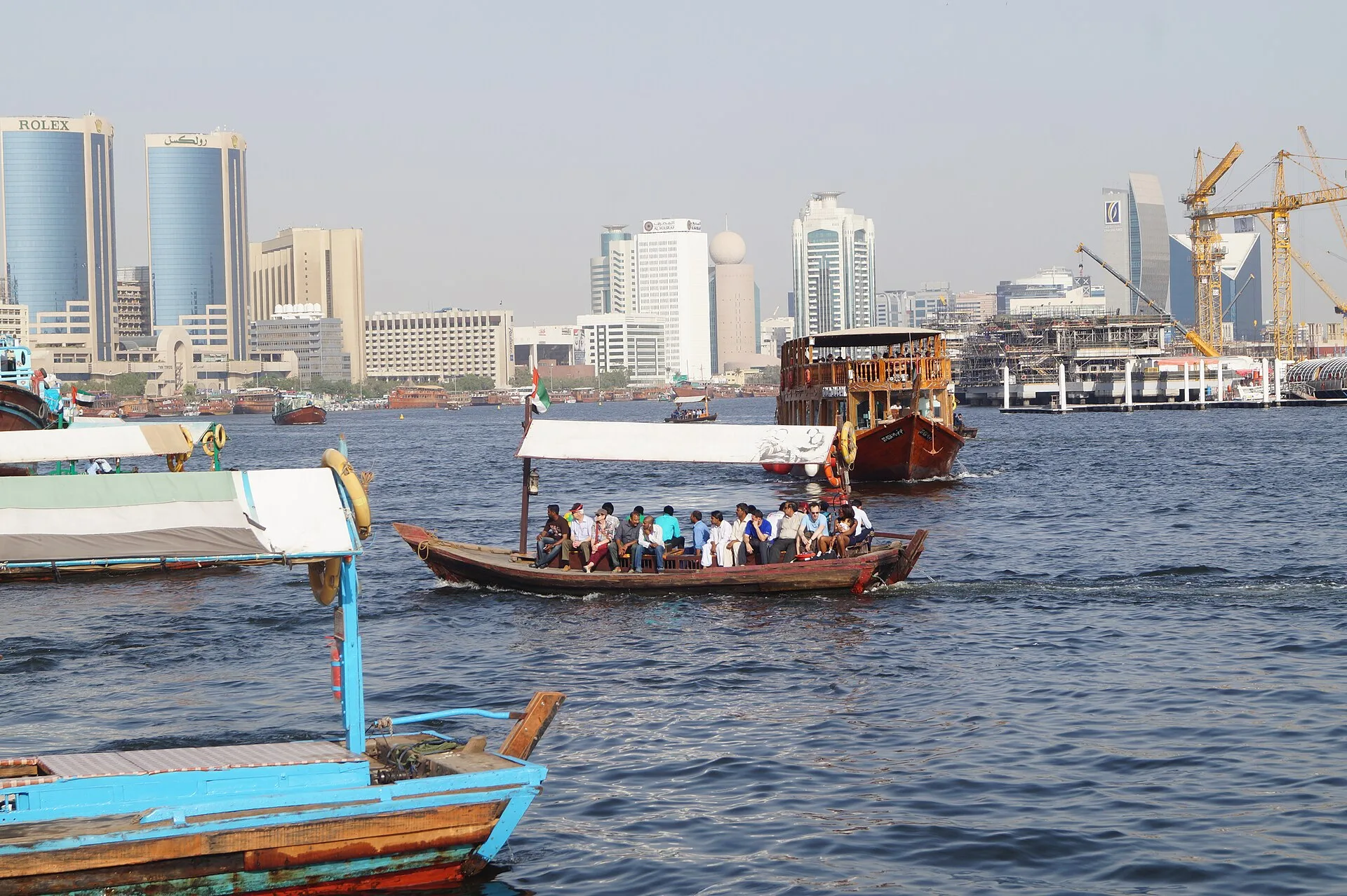 Wooden boats carrying passengers across a creek below city towers