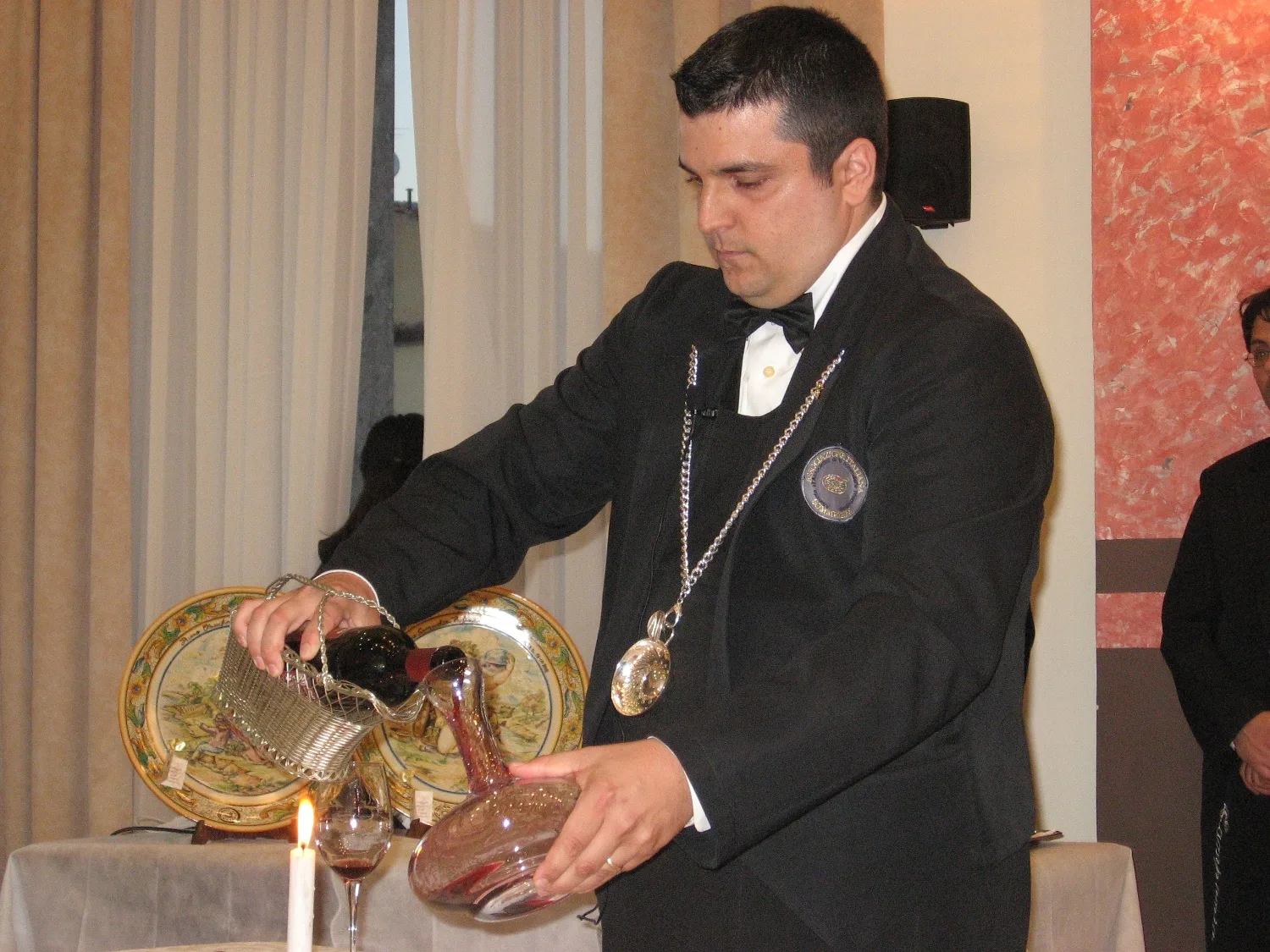Sommelier in a black jacket pouring red wine into a decanter