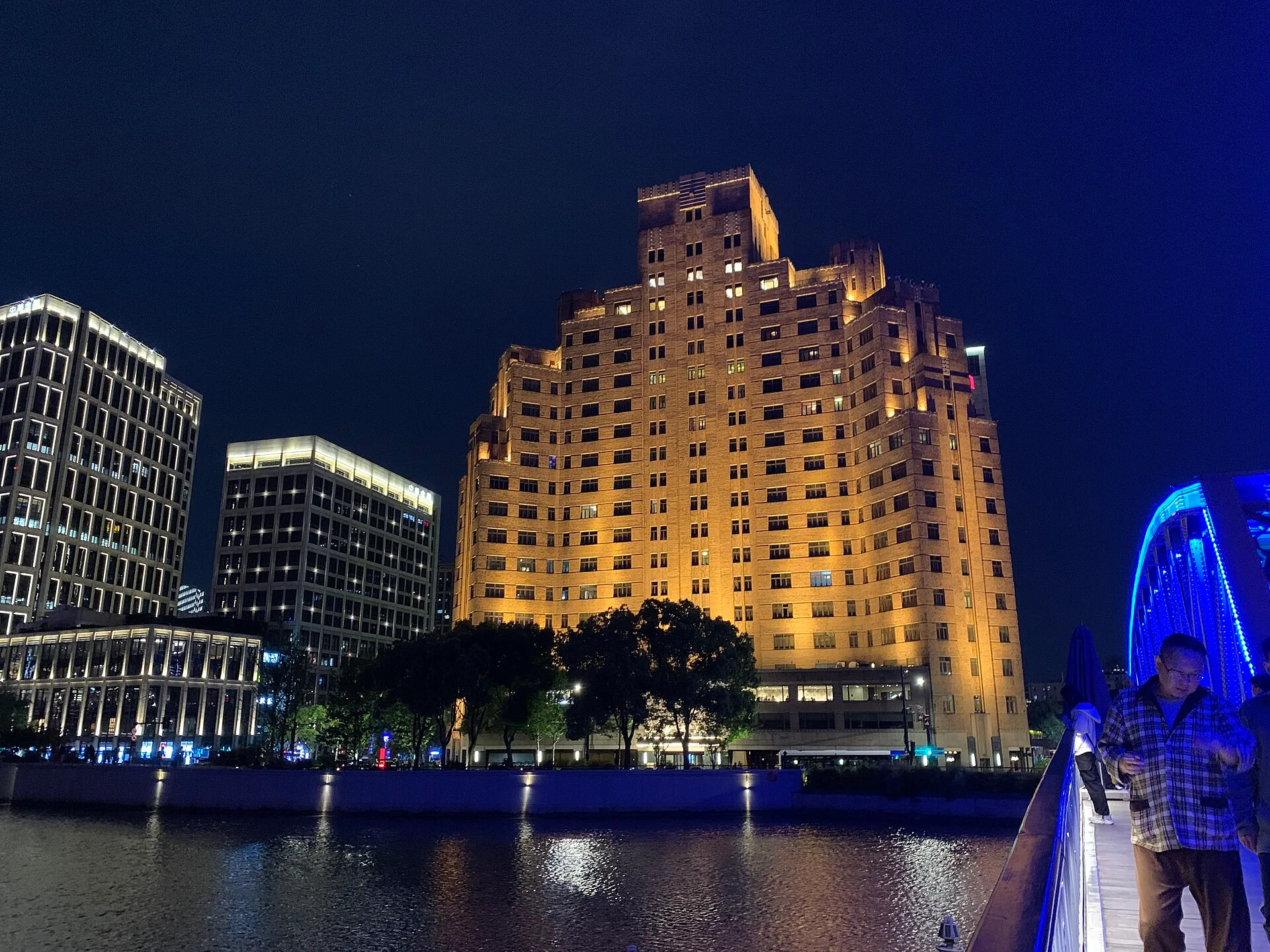 Stepped brick Art Deco tower lit up at night beside a river