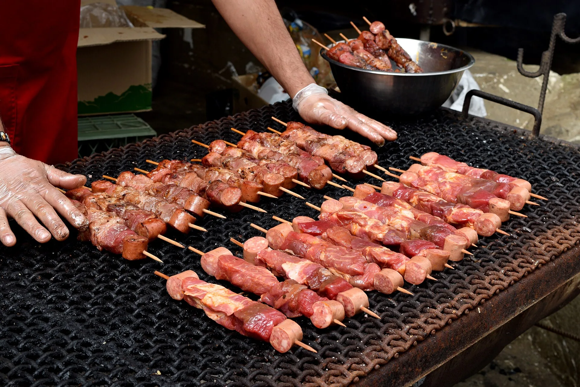 Rows of skewered meat cooking on a black metal grill