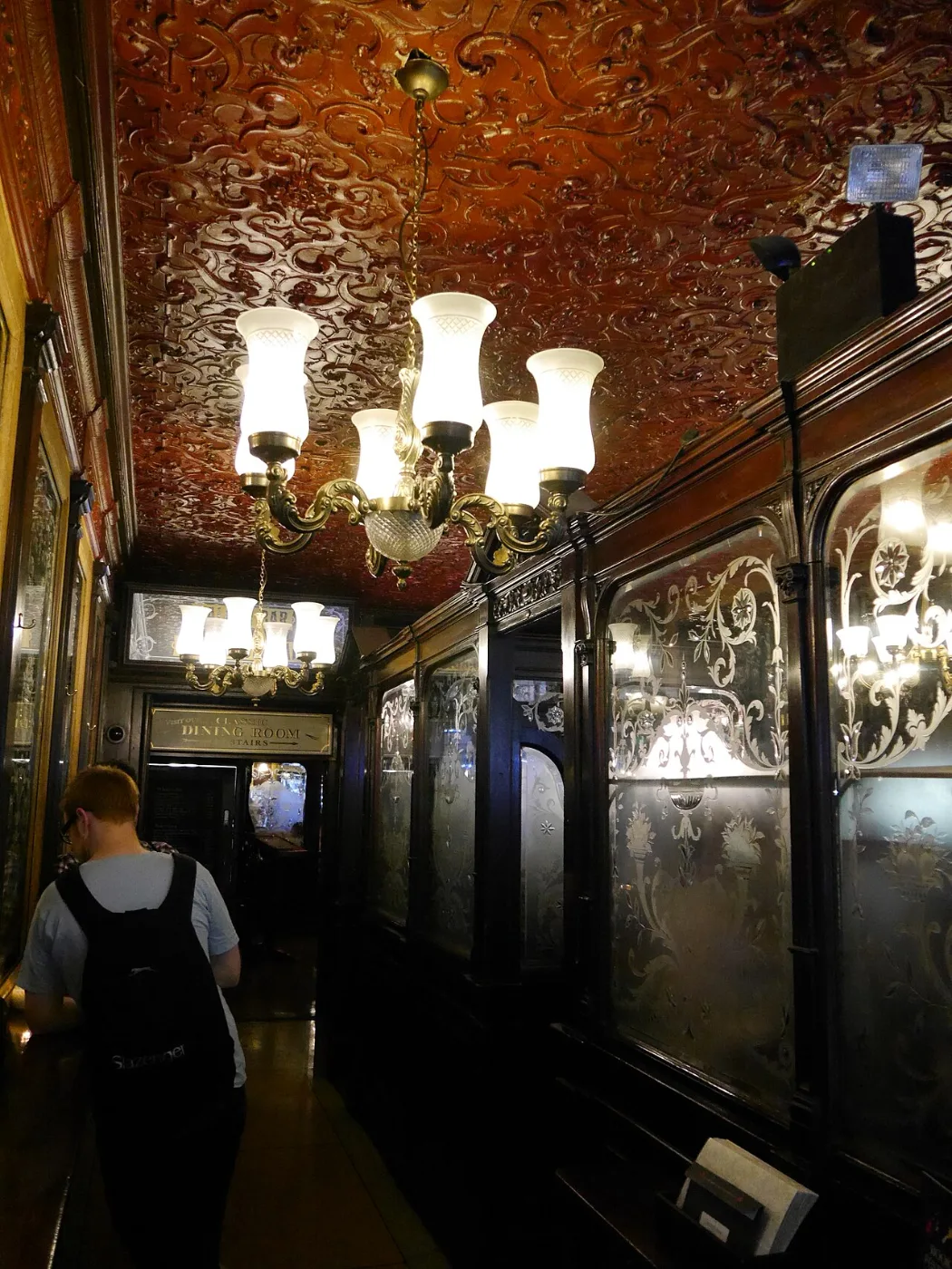 Narrow pub corridor lined with dark wood, decorated mirrors and glass lamps