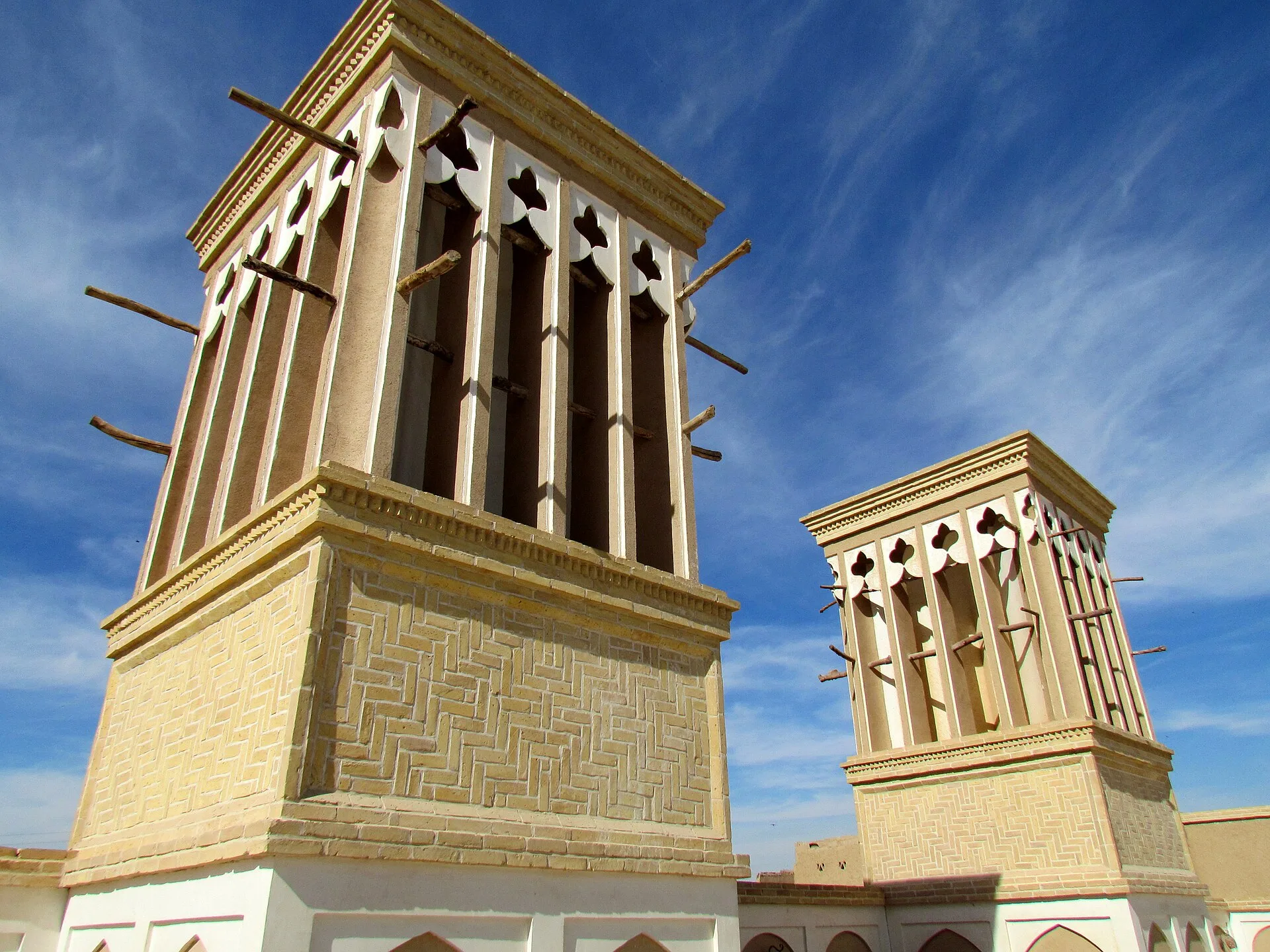 Two tall mud-brick windcatcher towers against a blue sky with clouds