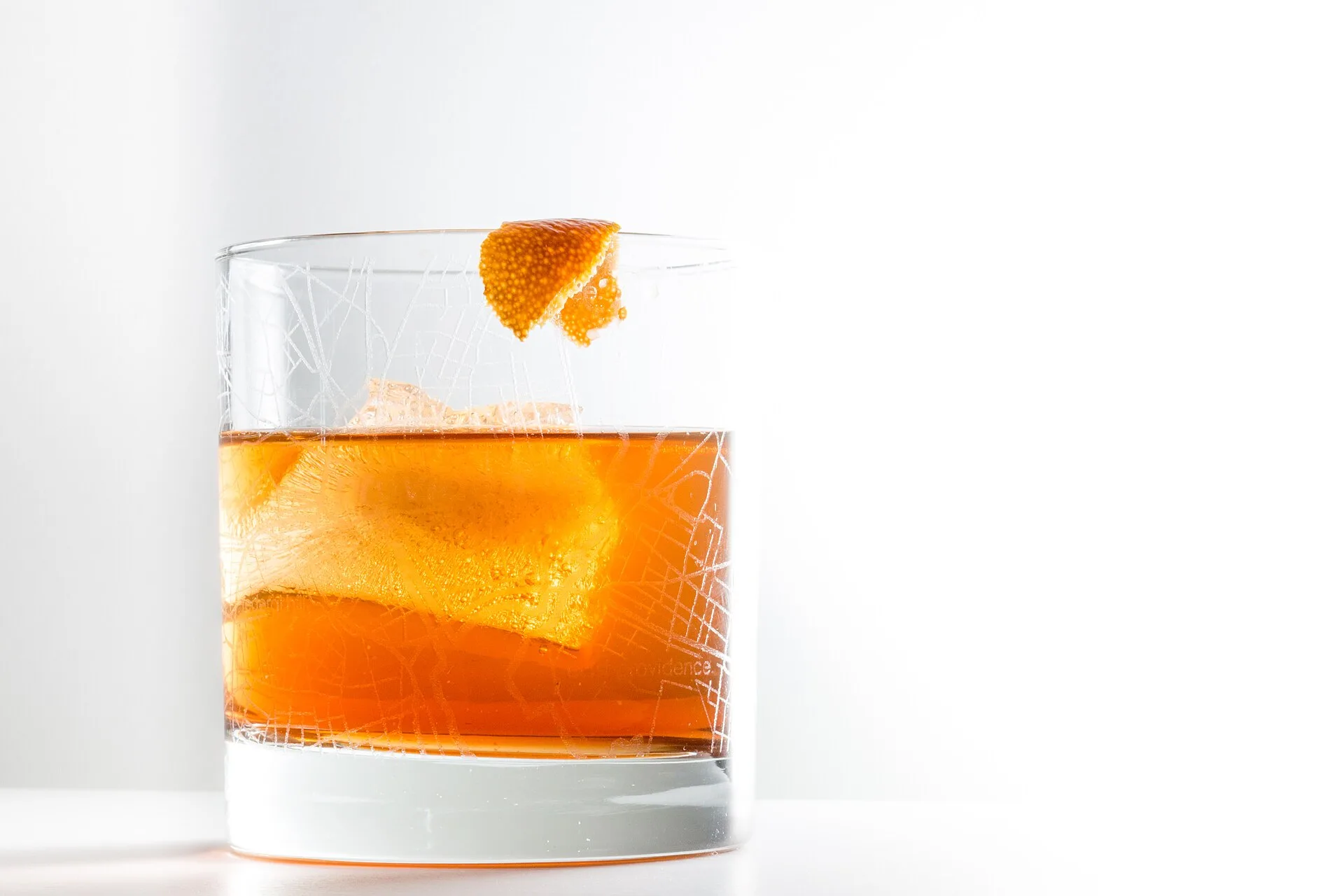 Amber cocktail over a large ice cube with an orange twist