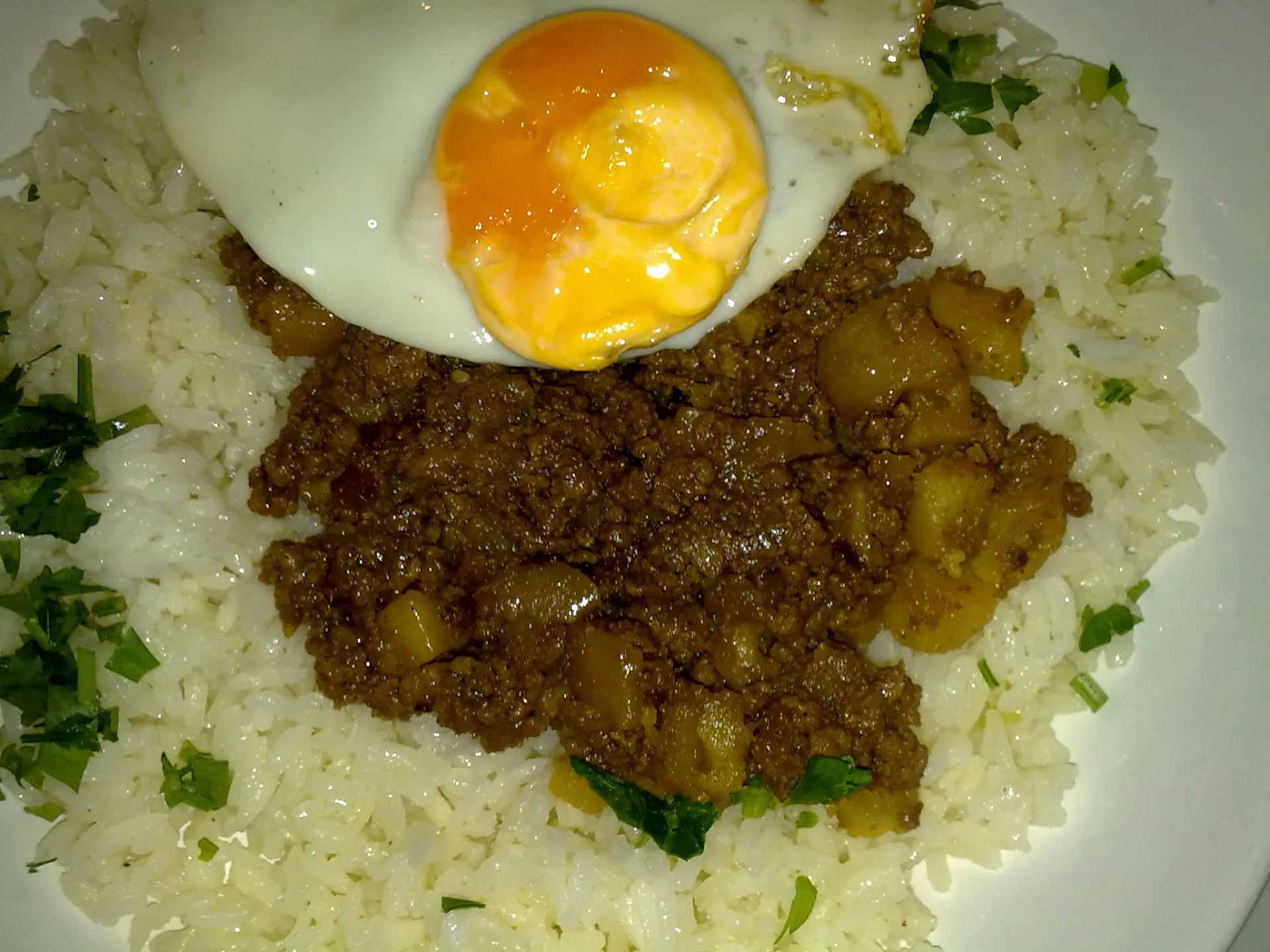 Minced meat with potato cubes on white rice topped with a fried egg